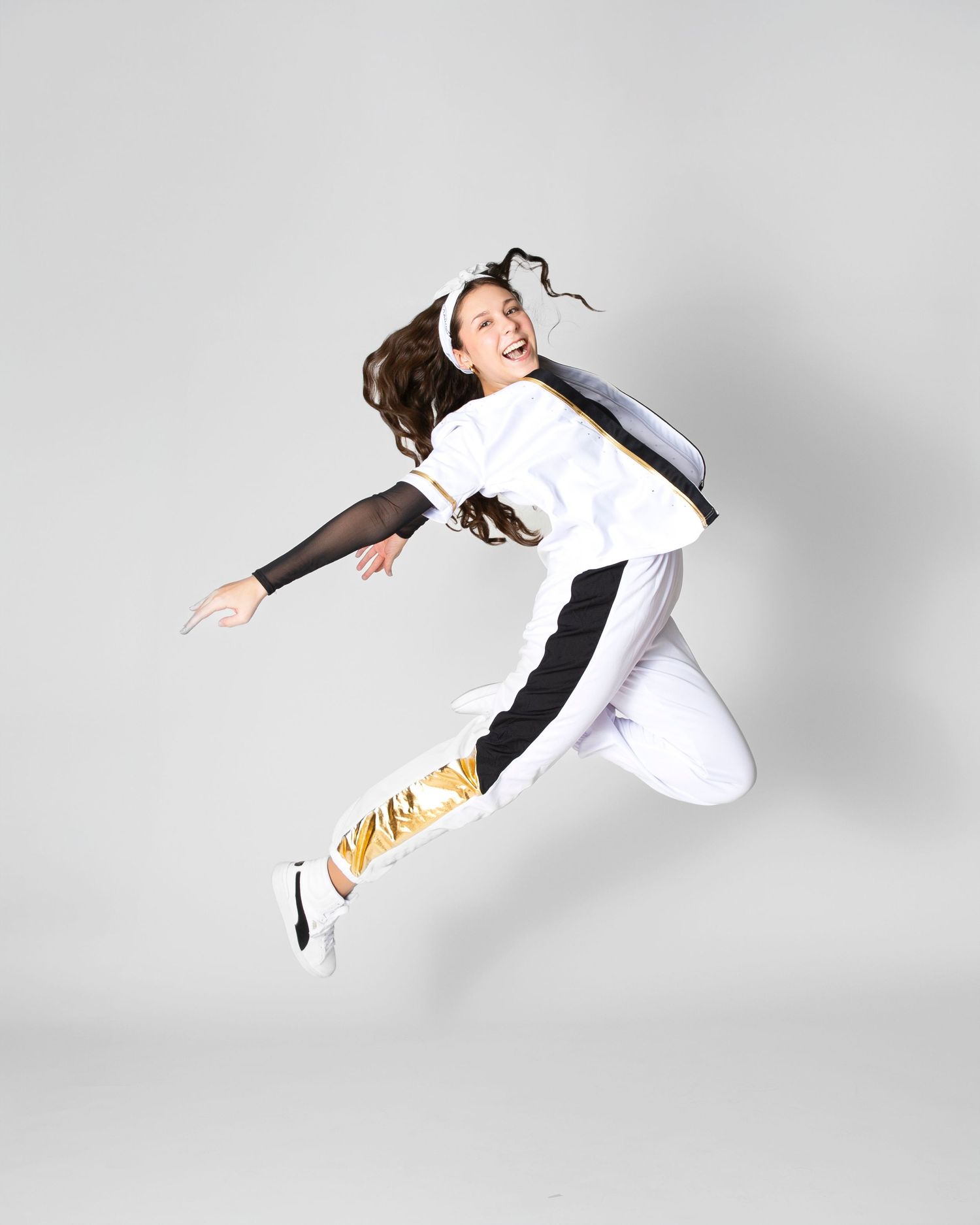 Dancer in white costume performs dynamic jumping sequence against white backdrop.