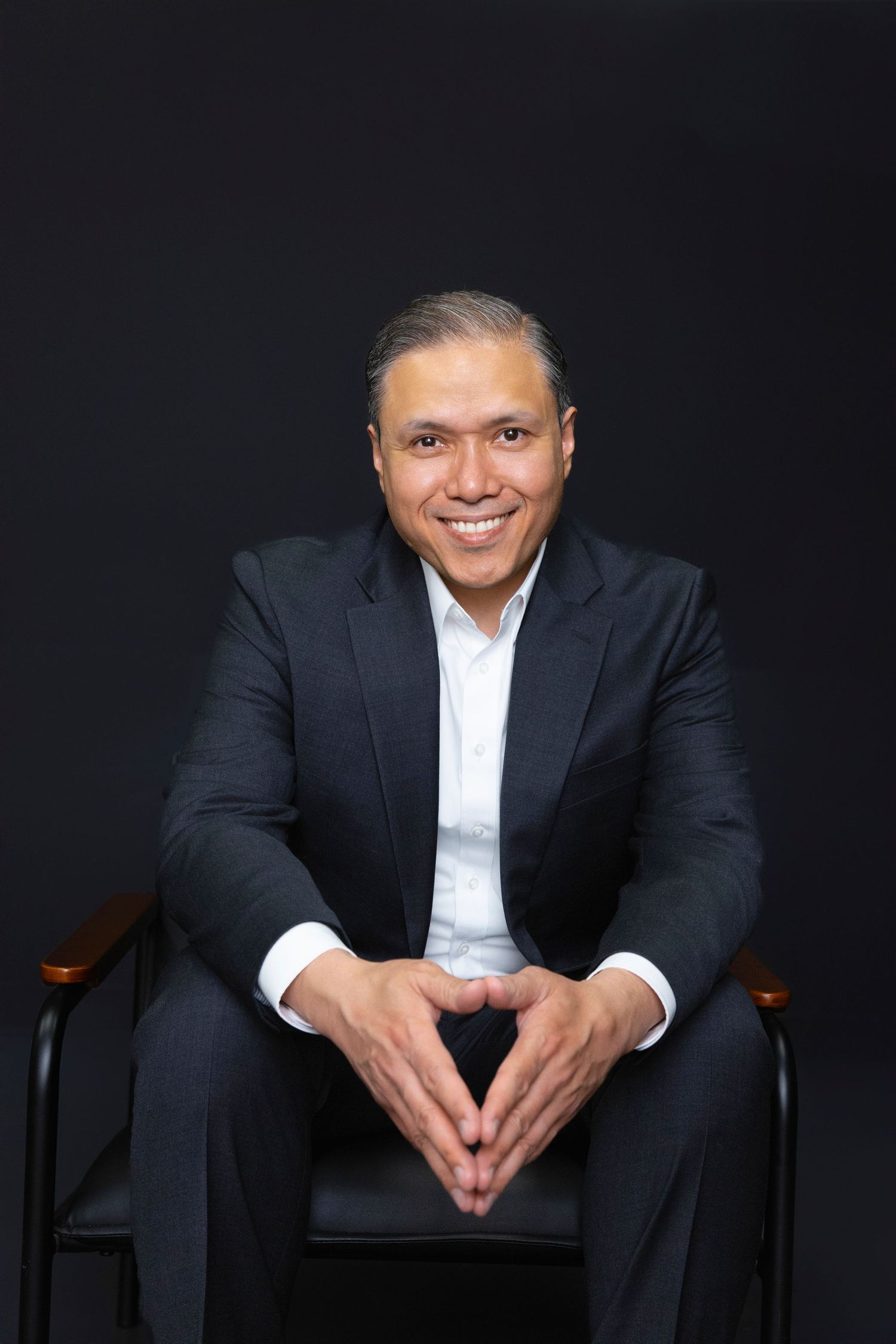 Business portraits of person in dark suit and white shirt against black background.