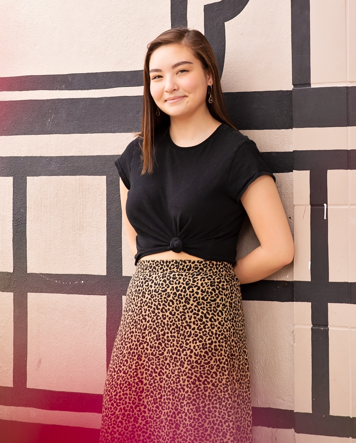 Modern fashion senior session portrait with black top and animal print skirt against abstract wall art.