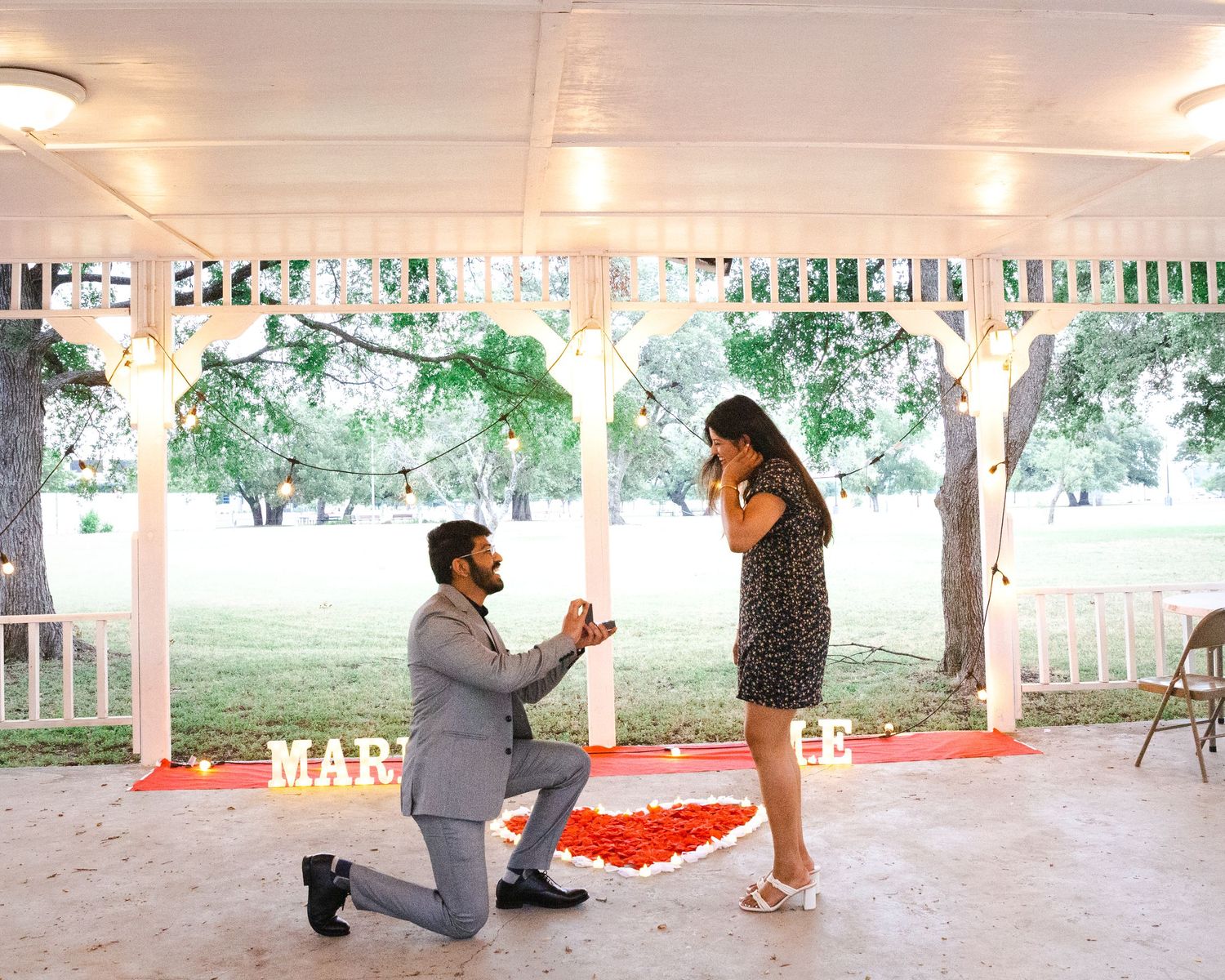 Romantic proposal scene under white gazebo with red heart decorations.
