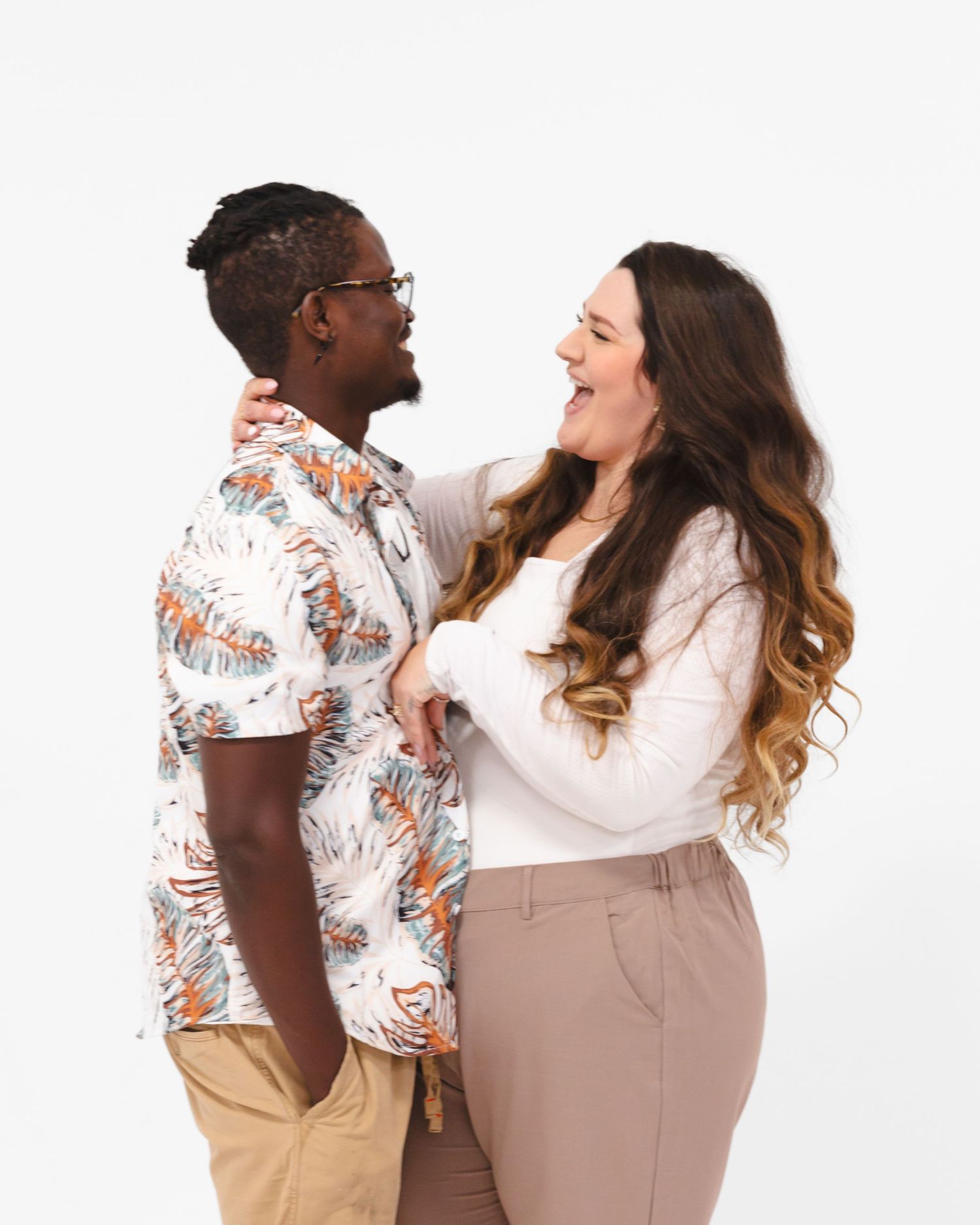Couple in casual attire poses against white background in studio setting.