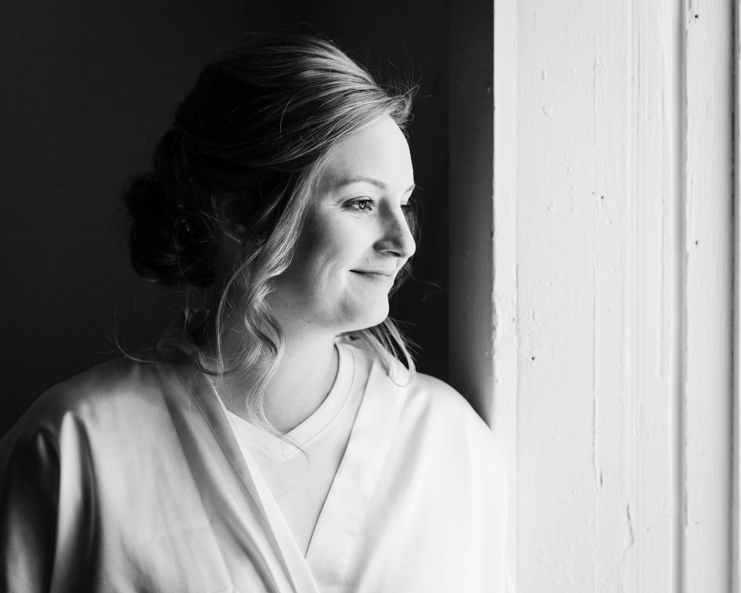 Black and white portrait of someone in a robe looking pensively out a window.