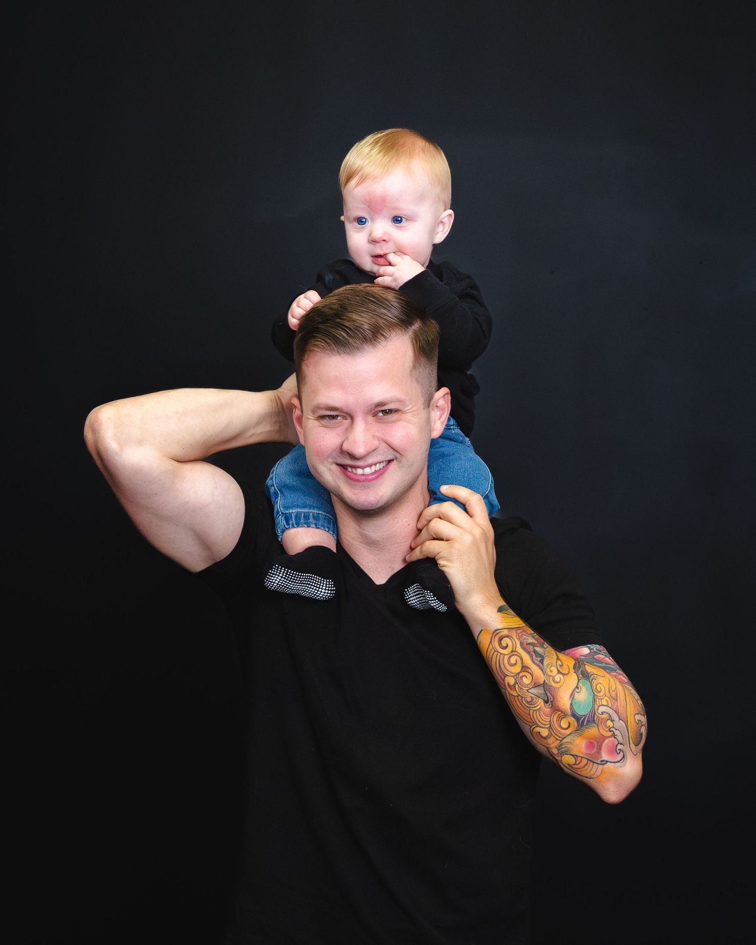 A person holds a toddler on their shoulders against a dark background.