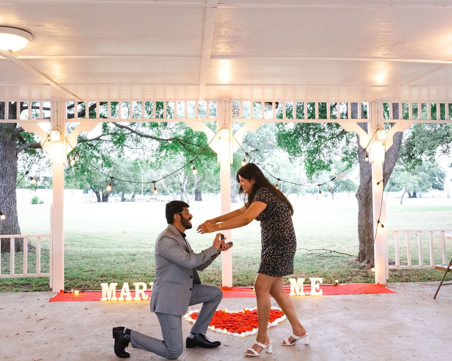 Romantic proposal scene under a white gazebo with string lights.