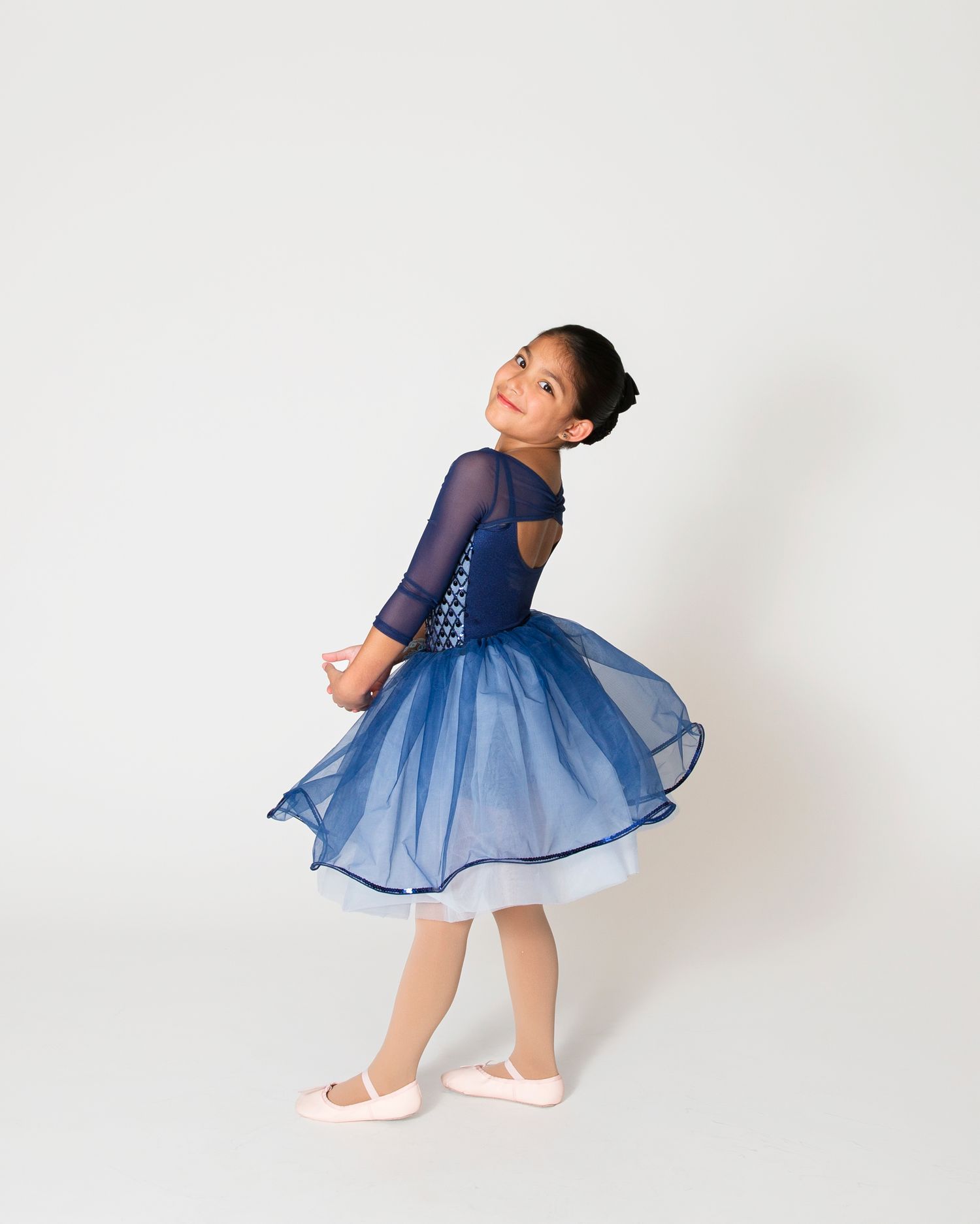 Ballet dancer in navy blue tutu dress twirls elegantly in studio.
