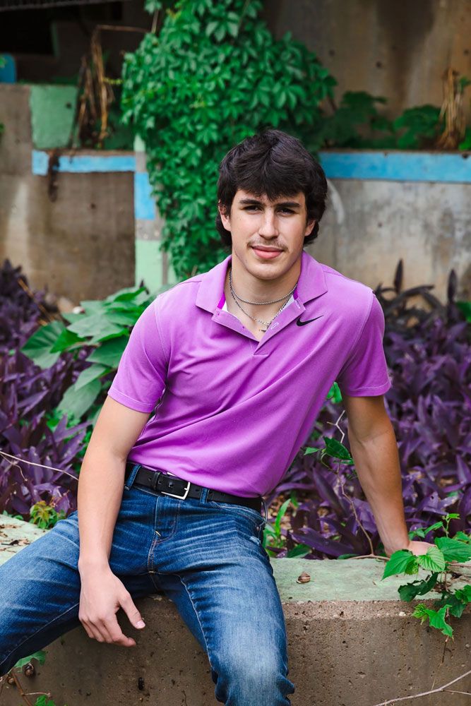 Casual outdoor portraits in purple polo shirt and jeans among garden foliage.