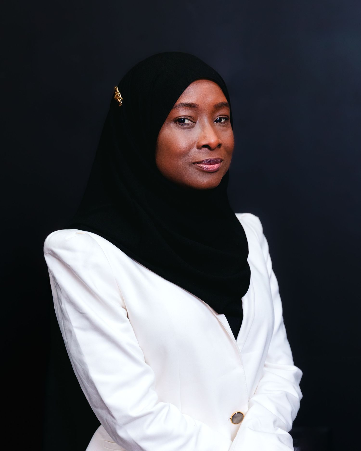 Professional studio portraits of person in white top and black hijab against dark background.