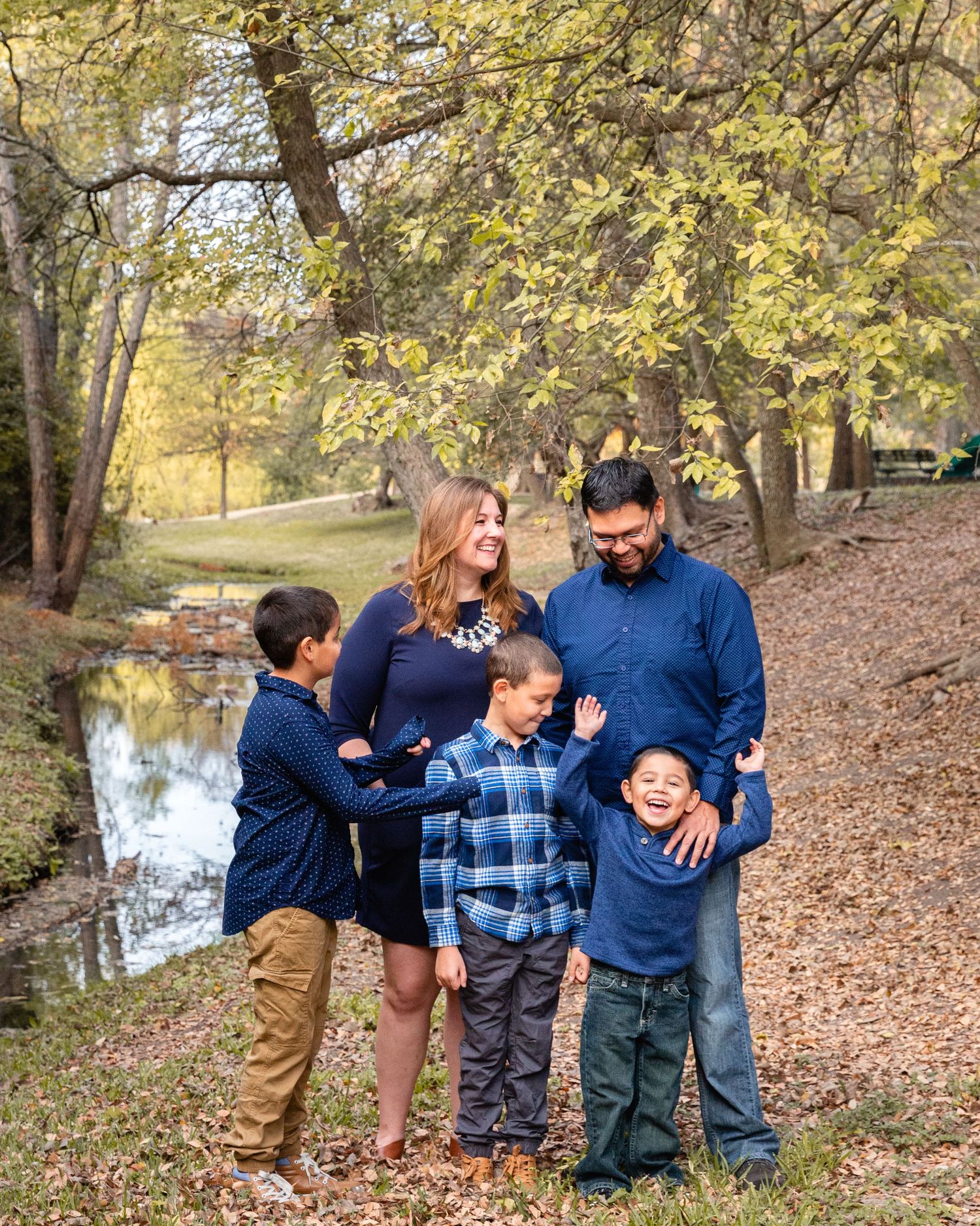 Family in coordinated blue outfits laughing together by autumn pond.