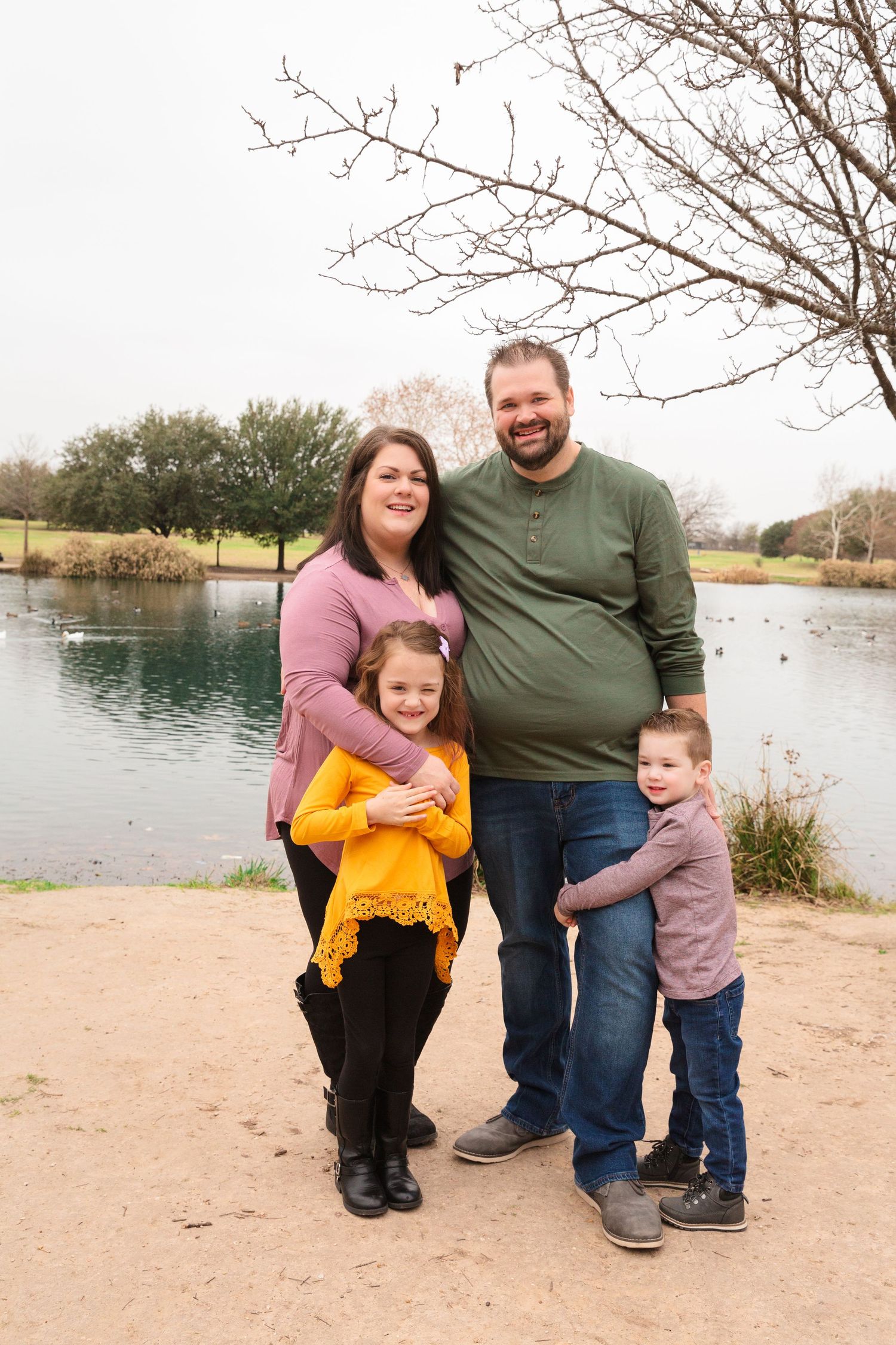 A family portrait session by a lake with bare winter trees in the background.
