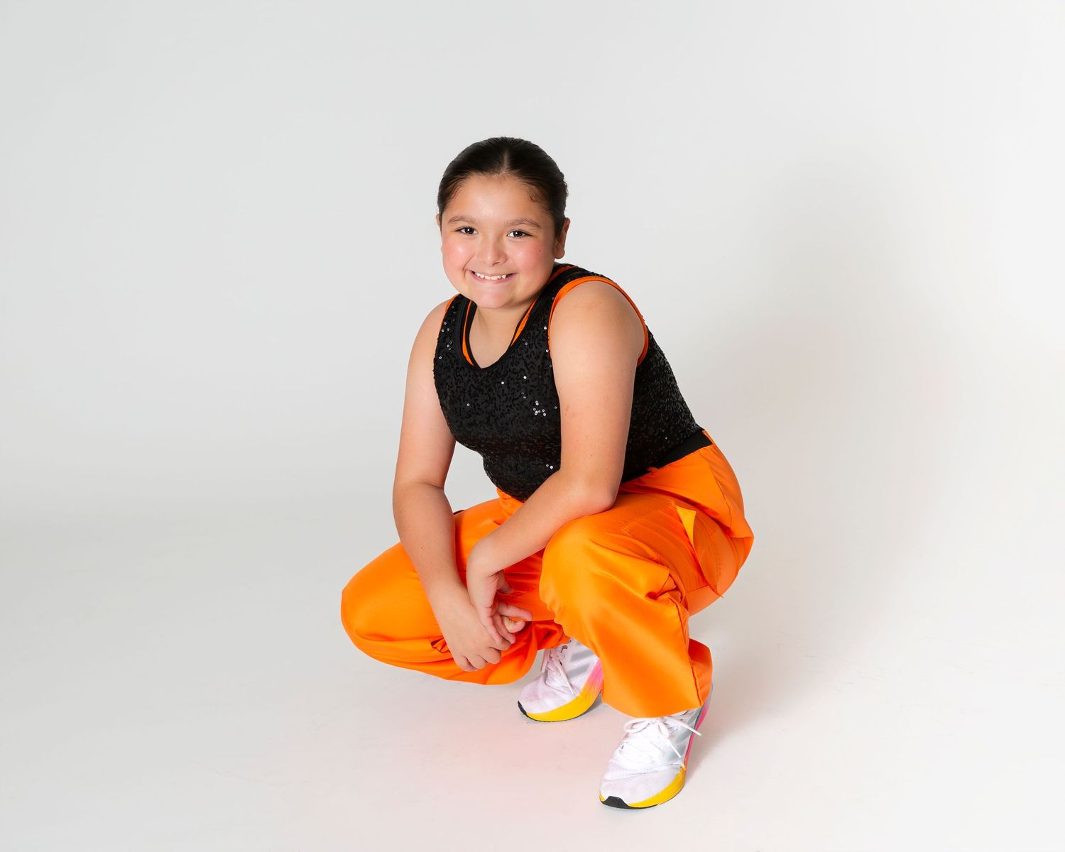 Dancer in orange pants striking dynamic pose against white background.