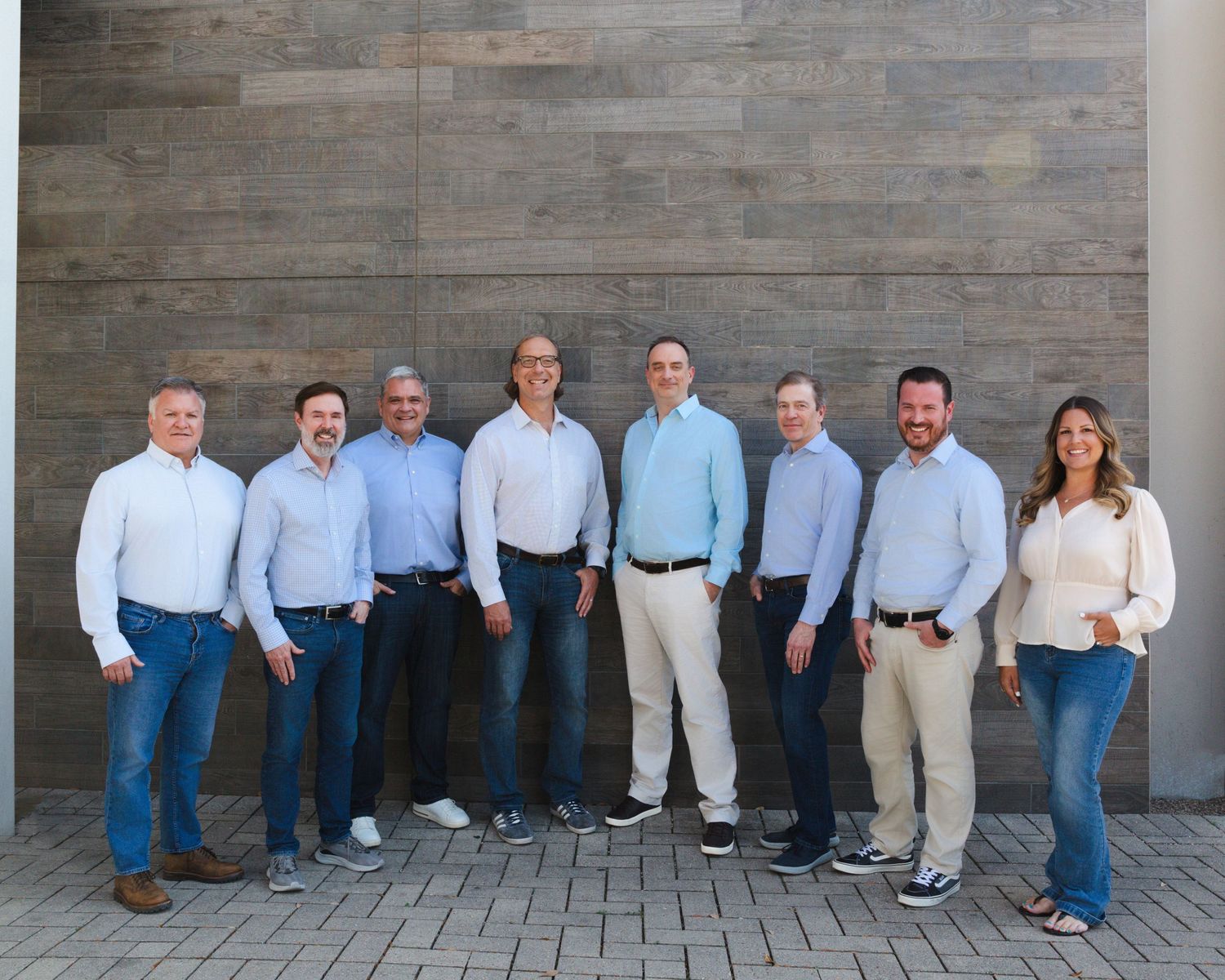 Group photo of business professionals standing against stone wall outdoors.