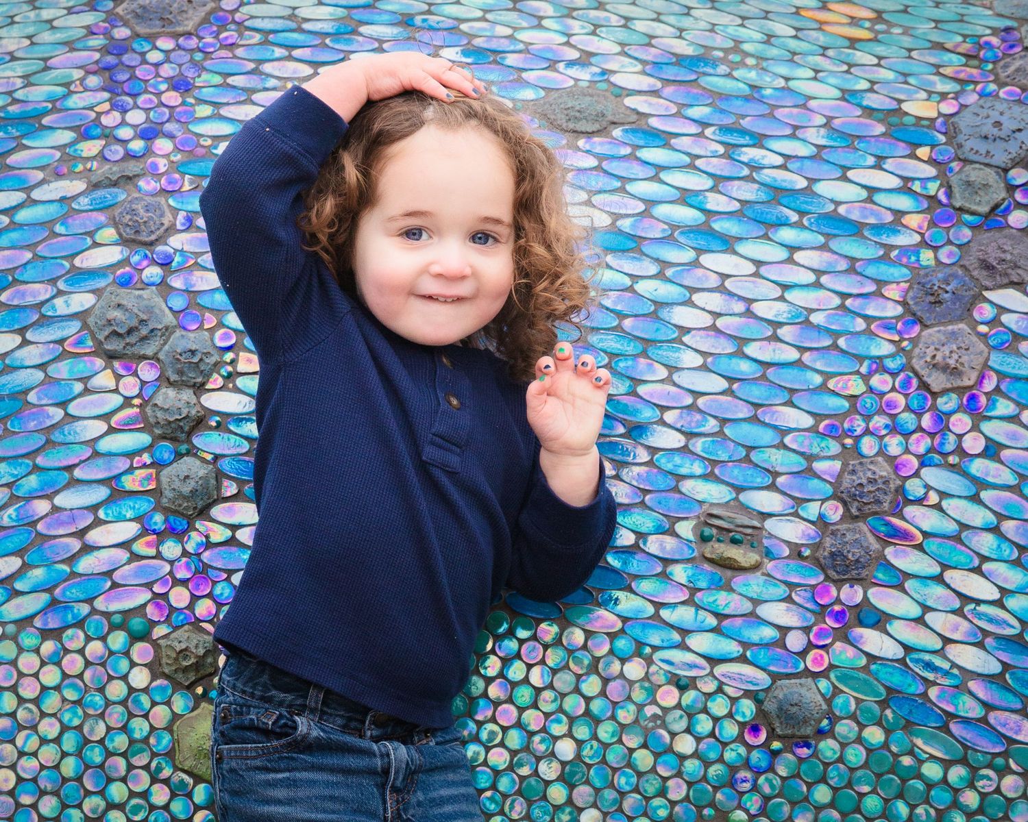 Child in navy blue sweater poses playfully on colorful mosaic background.