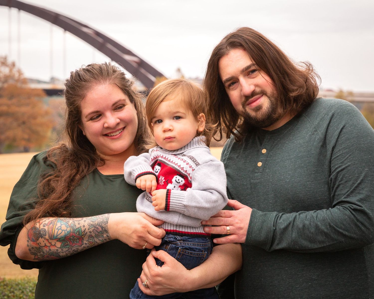 Casual family portraits outdoors featuring parents with small child in autumn setting.