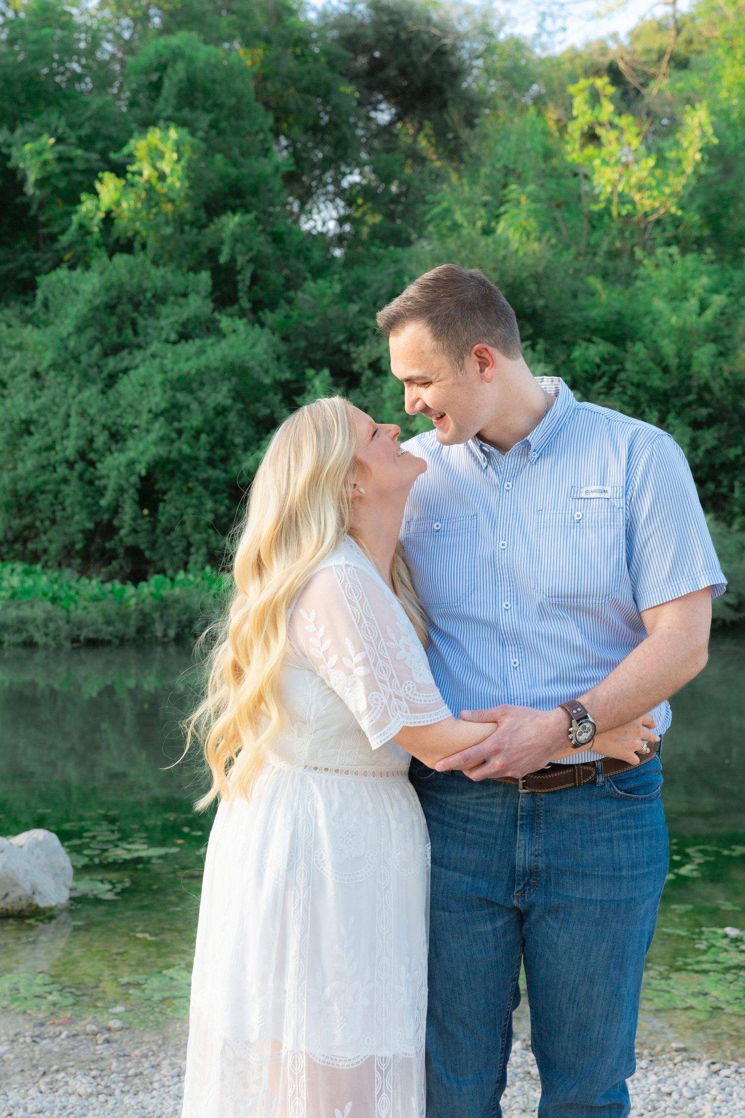 Couple in white and blue attire sharing tender moments near a lake.