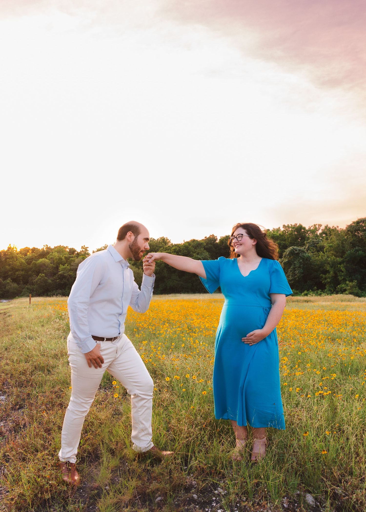 A couple shares playful moments in a wildflower field during their maternity photoshoot at sunset.