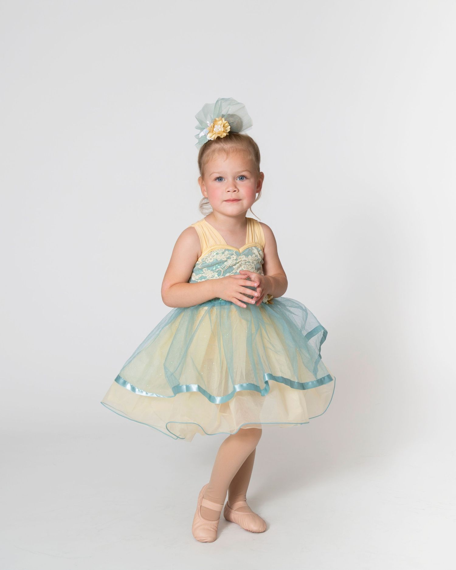 Dancer in mint and yellow tulle dress performs ballet movements in studio.