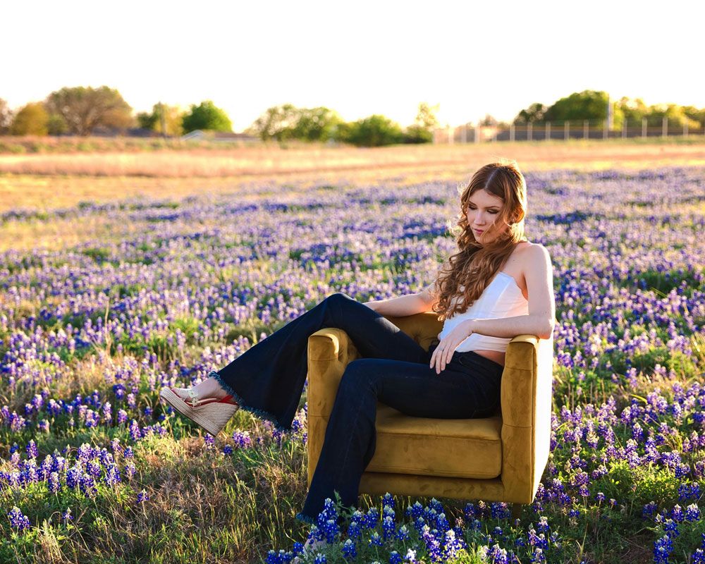 A reader relaxes in a yellow armchair surrounded by blooming bluebonnets in a Texas field.