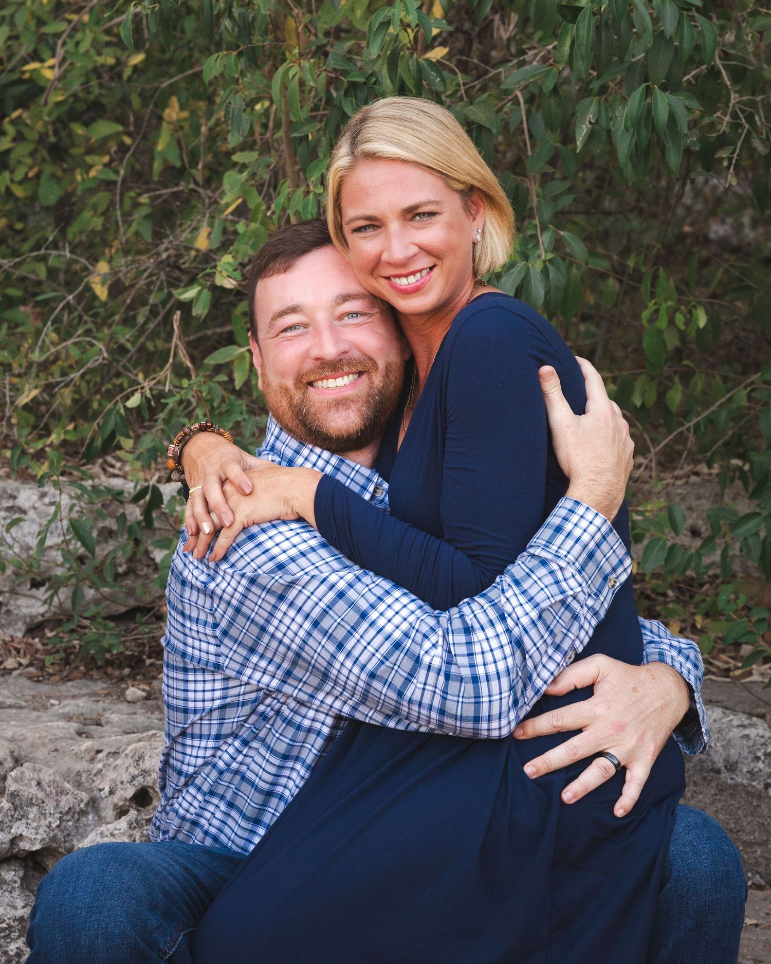 Couple in casual attire poses playfully on ground during outdoor photo session.