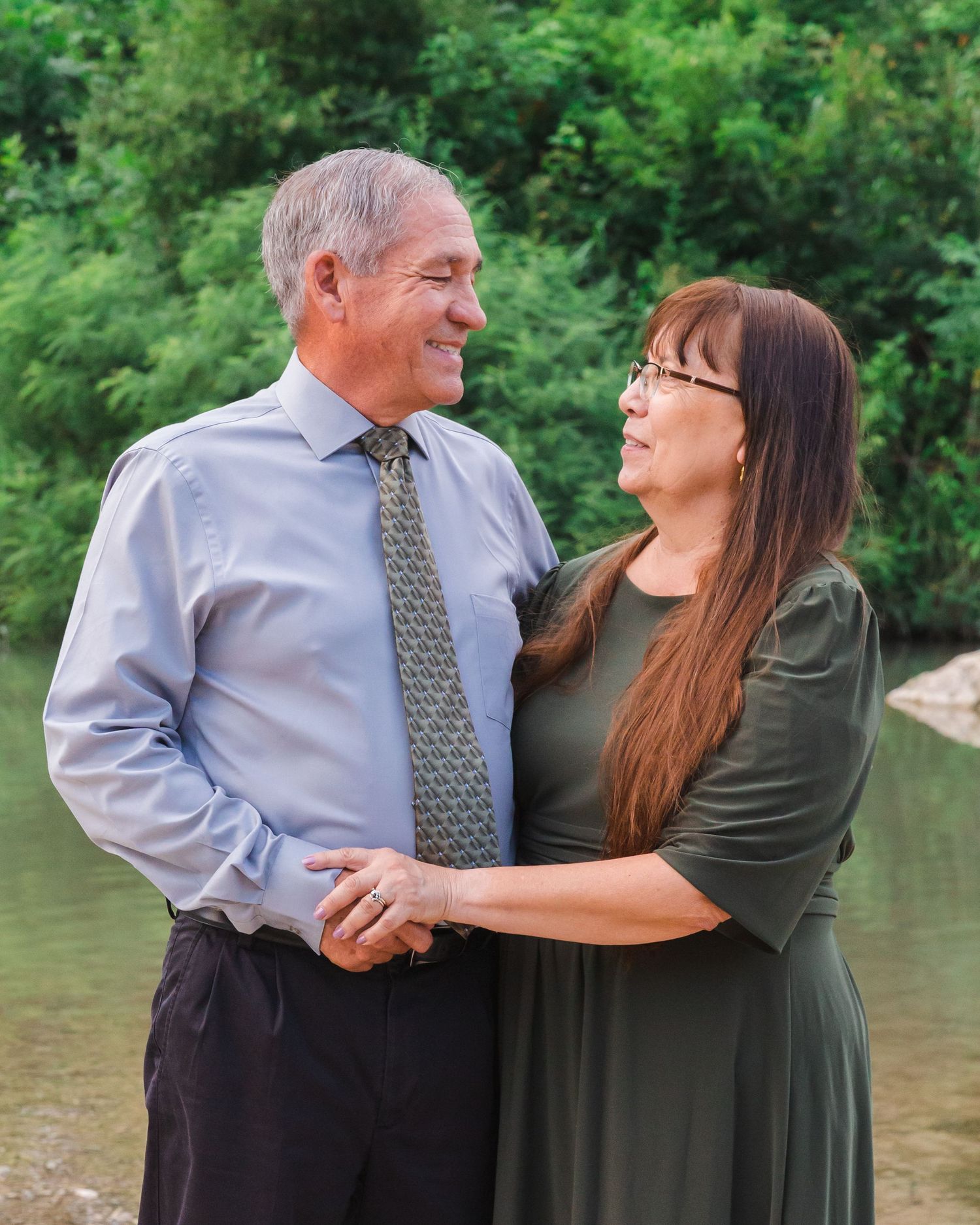 Couple dancing together by a lake surrounded by lush greenery.
