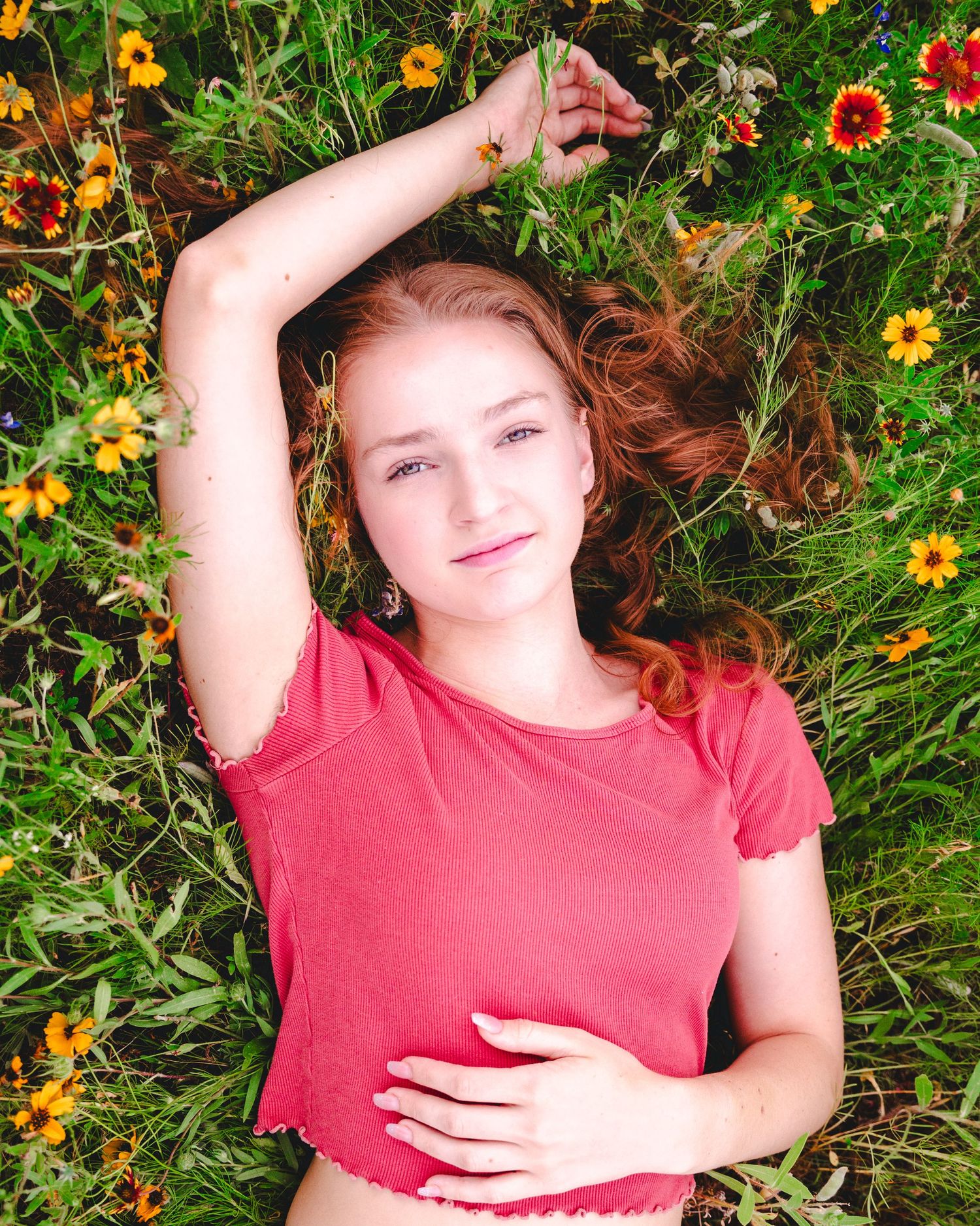 Young woman in red top lying in garden surrounded by yellow and orange flowers.
