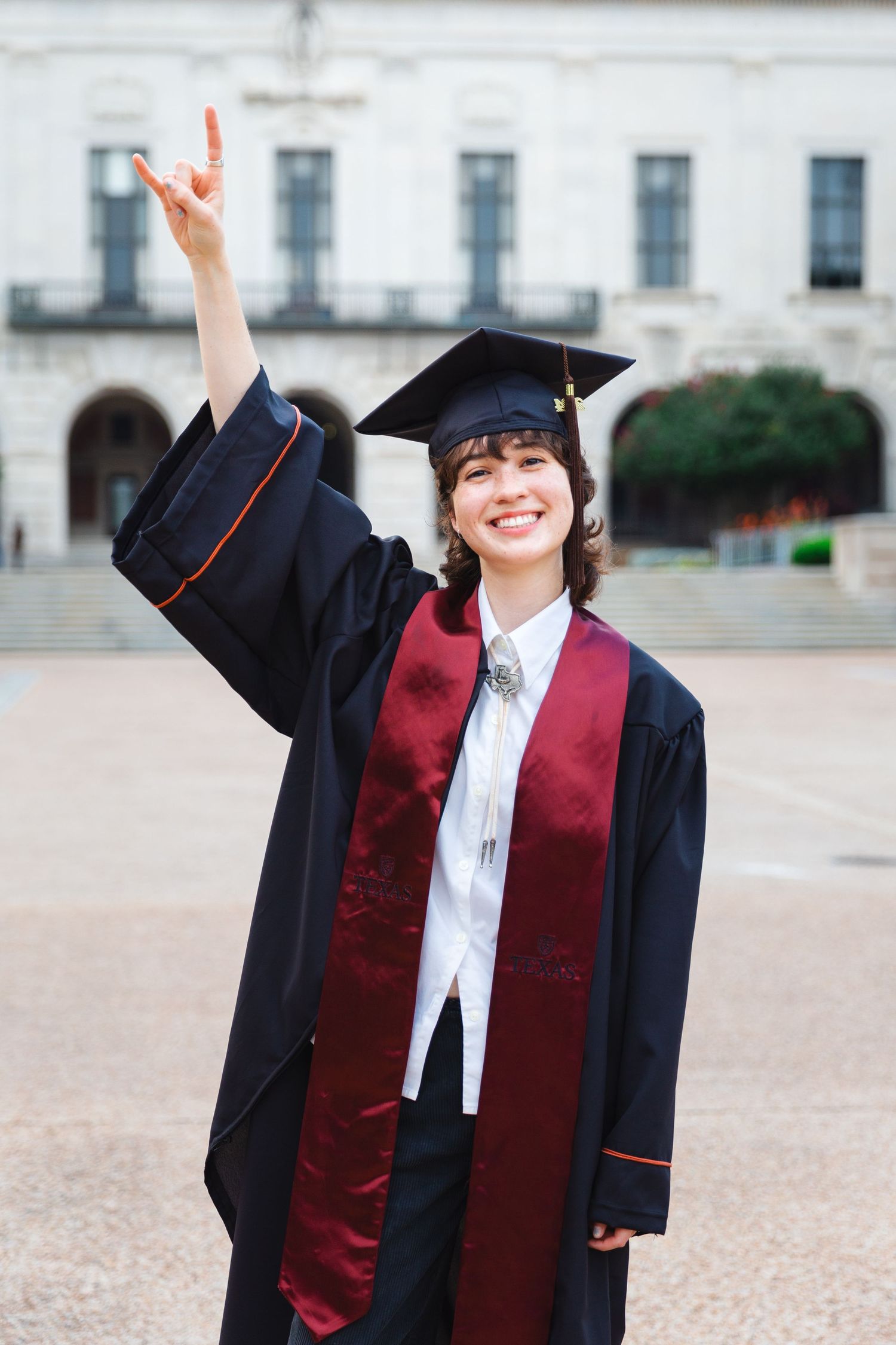 Graduate in cap and gown raises hand in celebration on campus.