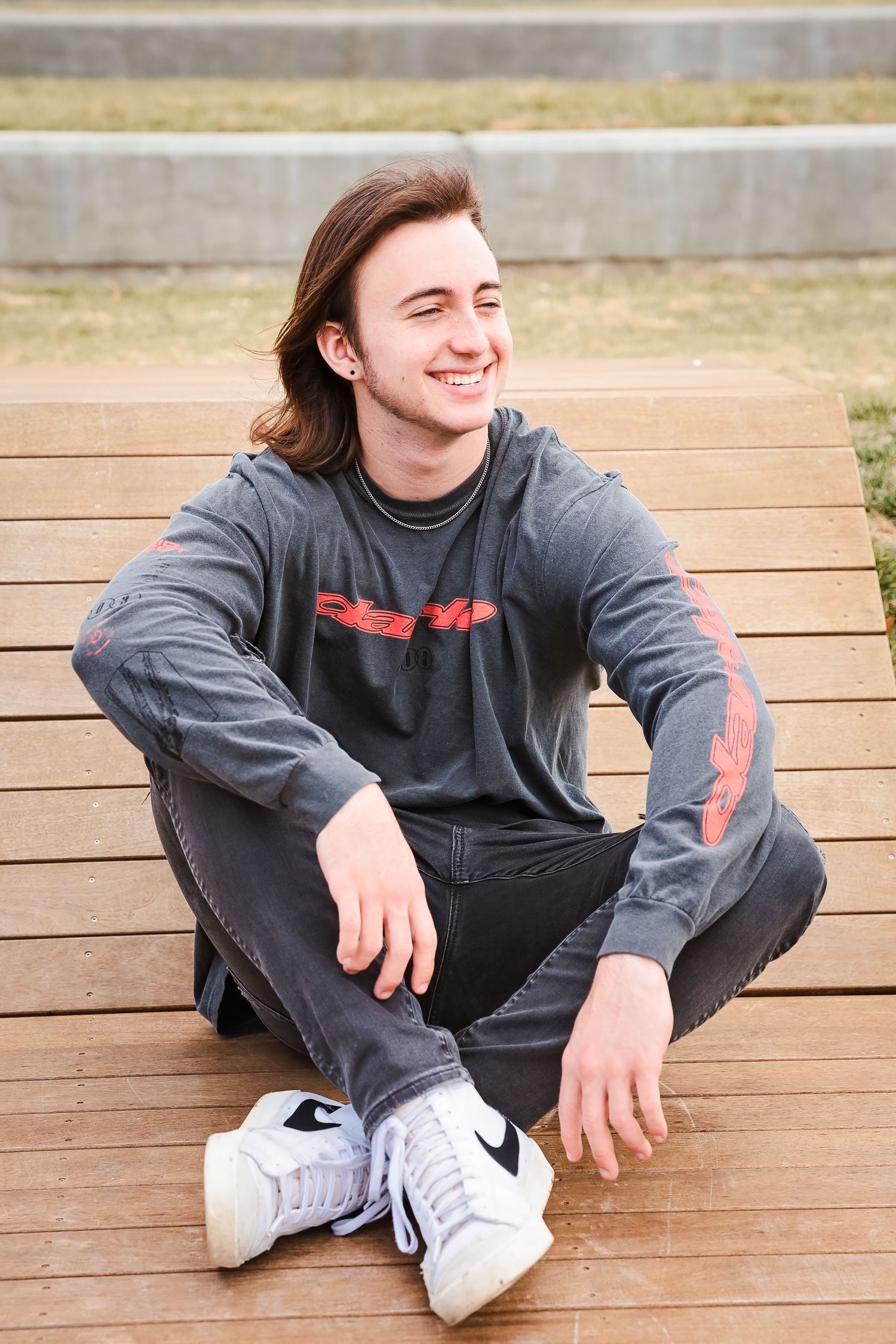 Person in gray sweatshirt relaxing on wooden deck during casual portrait session.