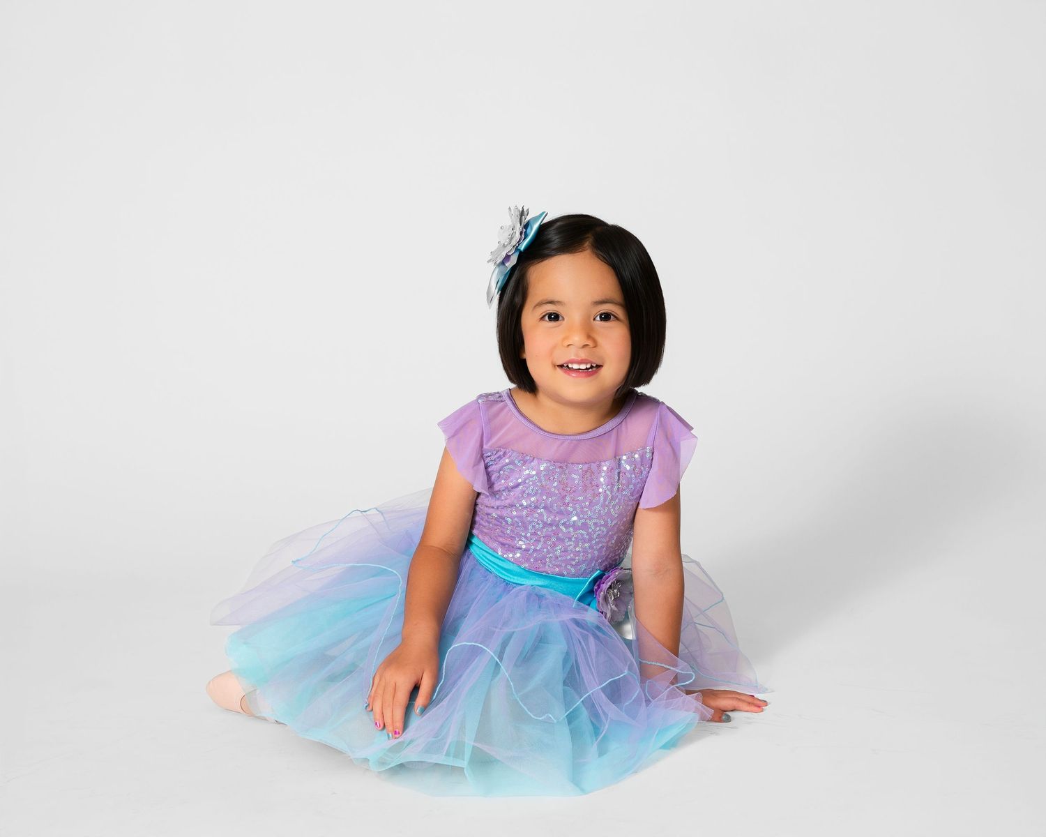 Dancer in purple and blue tulle dress performs graceful movements on white background.