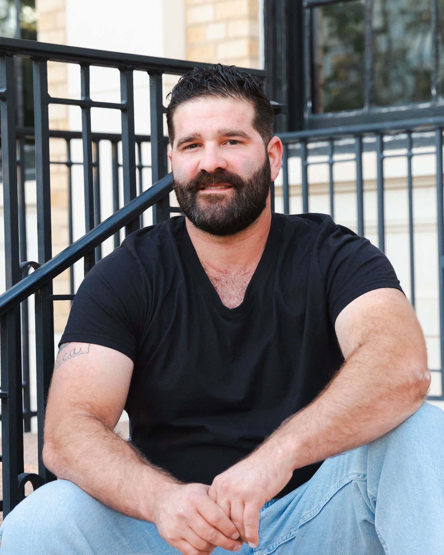 Casual outdoor portraits of someone in black t-shirt sitting by metal railing.