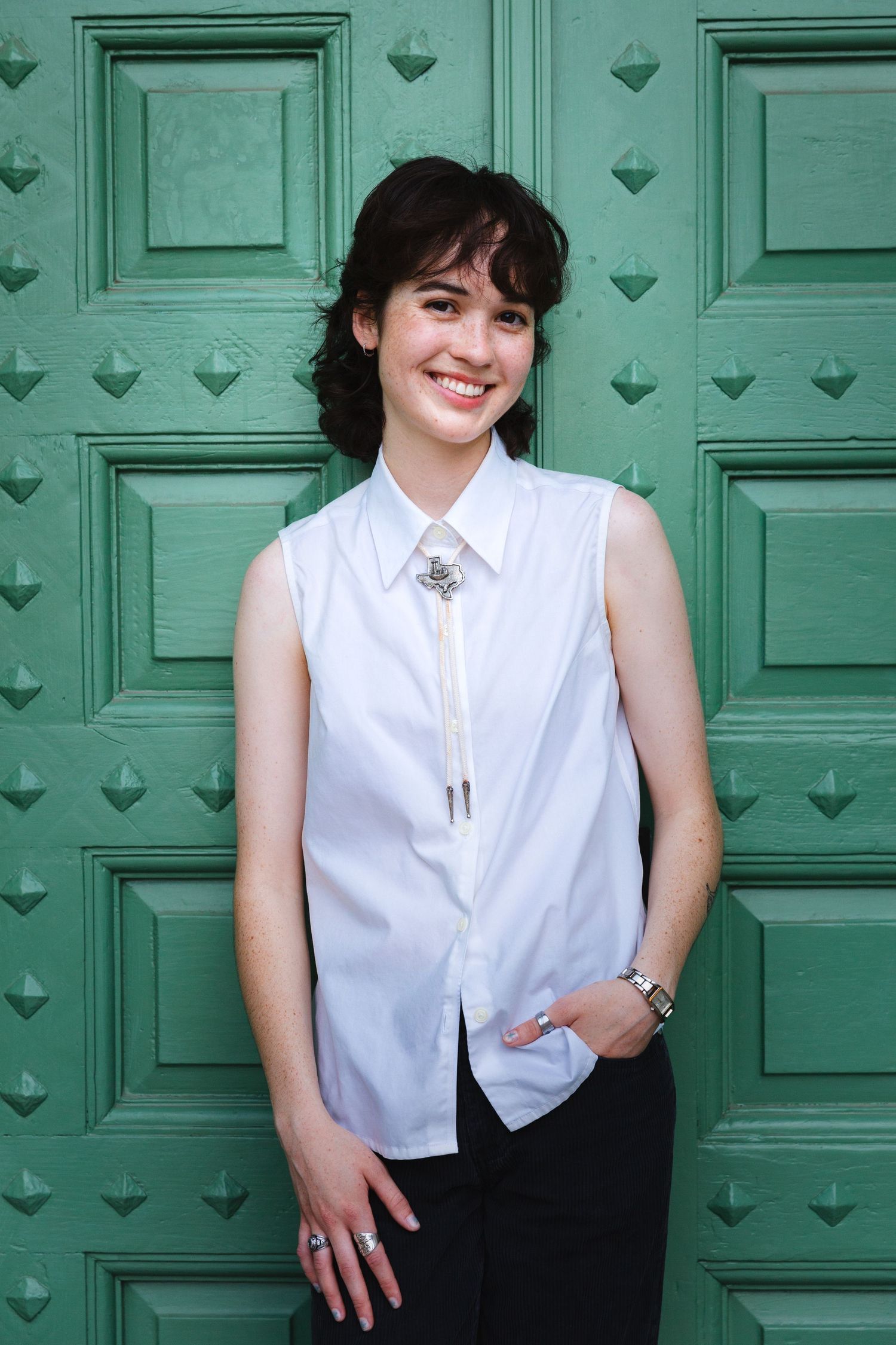 College graduate Portrait against green door wearing white sleeveless blouse with statement necklace. Senior portrait session UT Austin
