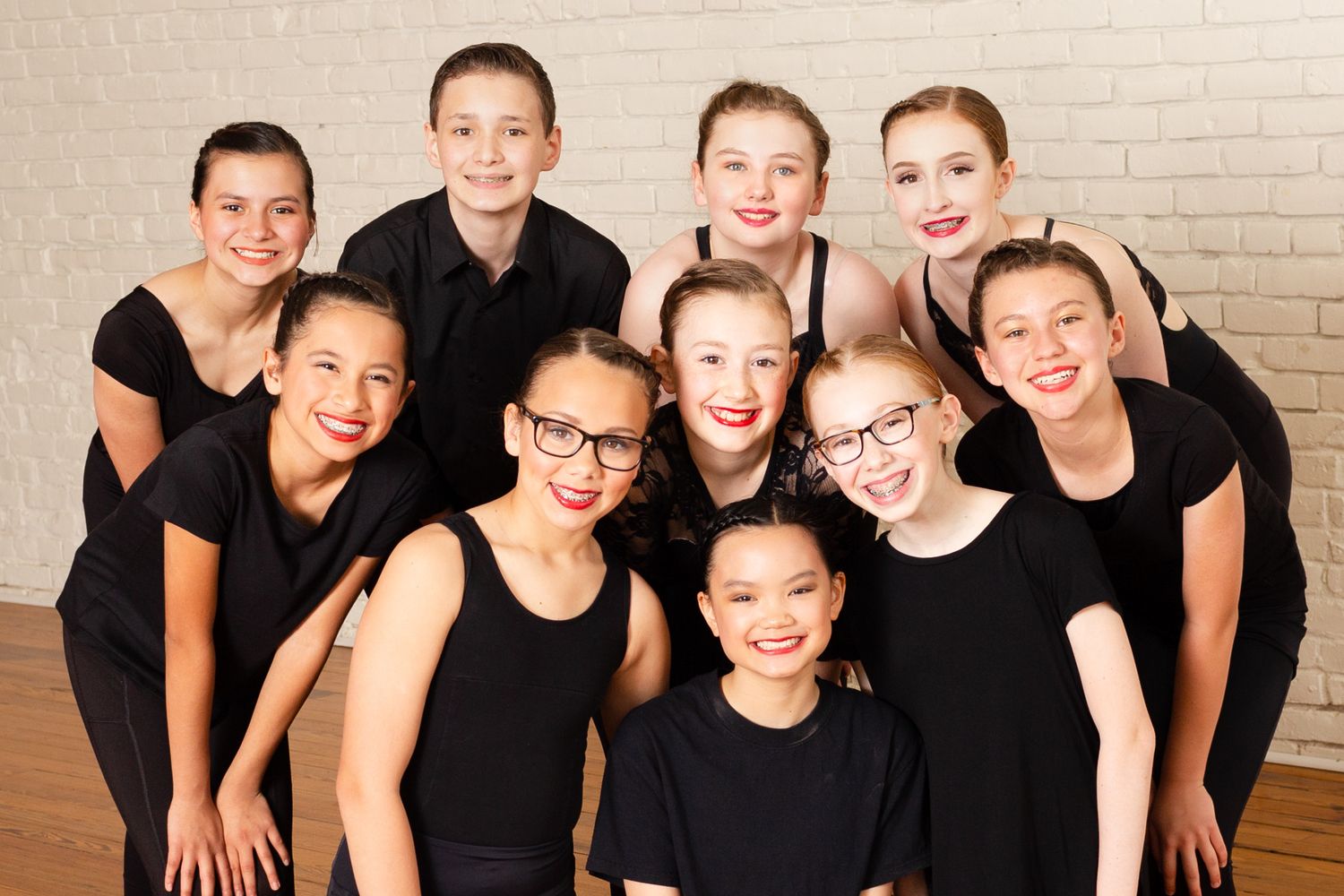 Group of young performers in black outfits posing together for a studio portrait.