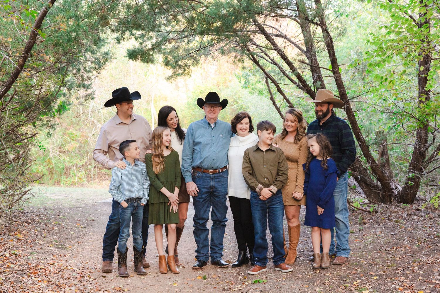 A group in western-style clothing poses together in a wooded outdoor setting at sunset.