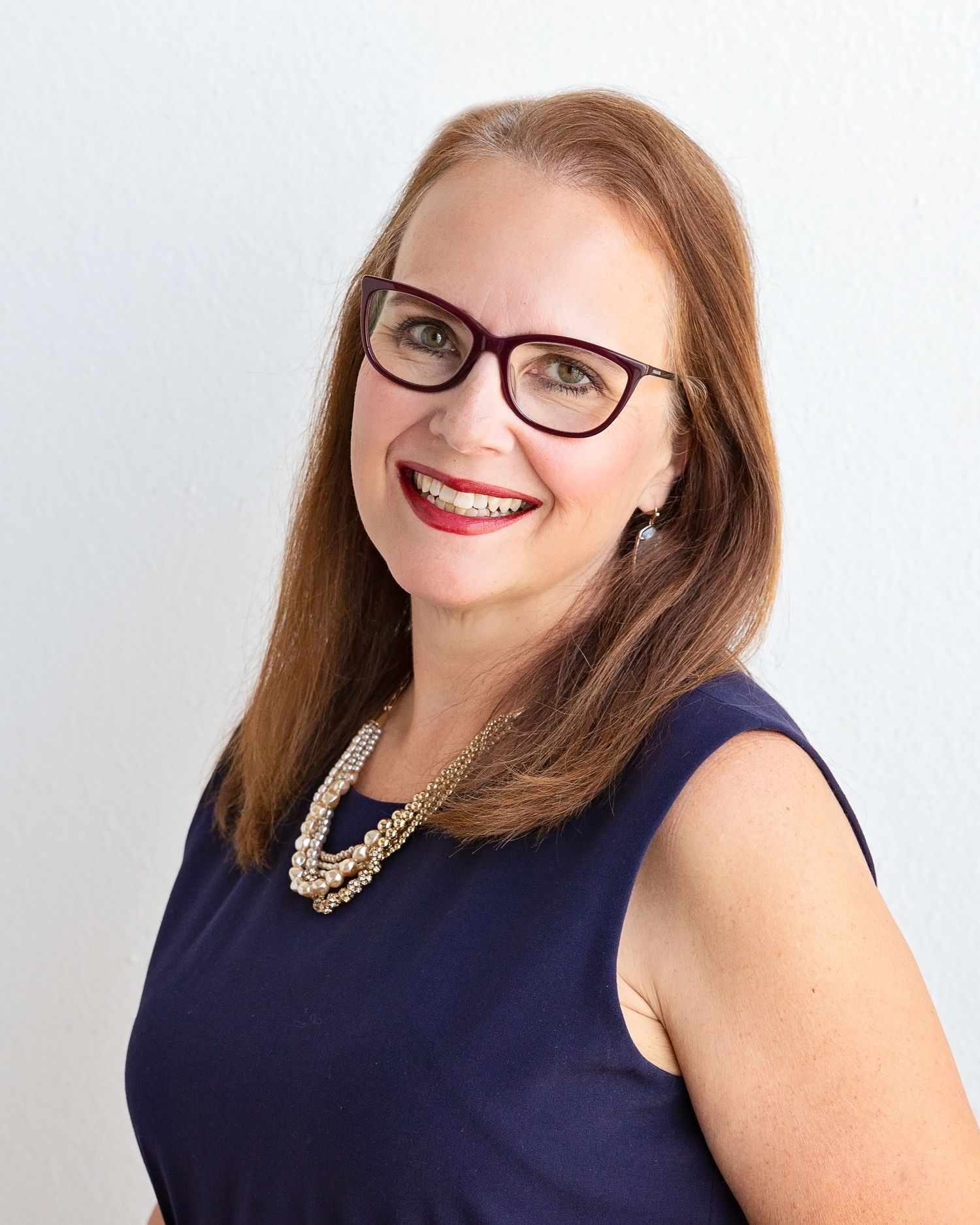 Professional headshots in a navy dress and statement necklace against white backdrop.