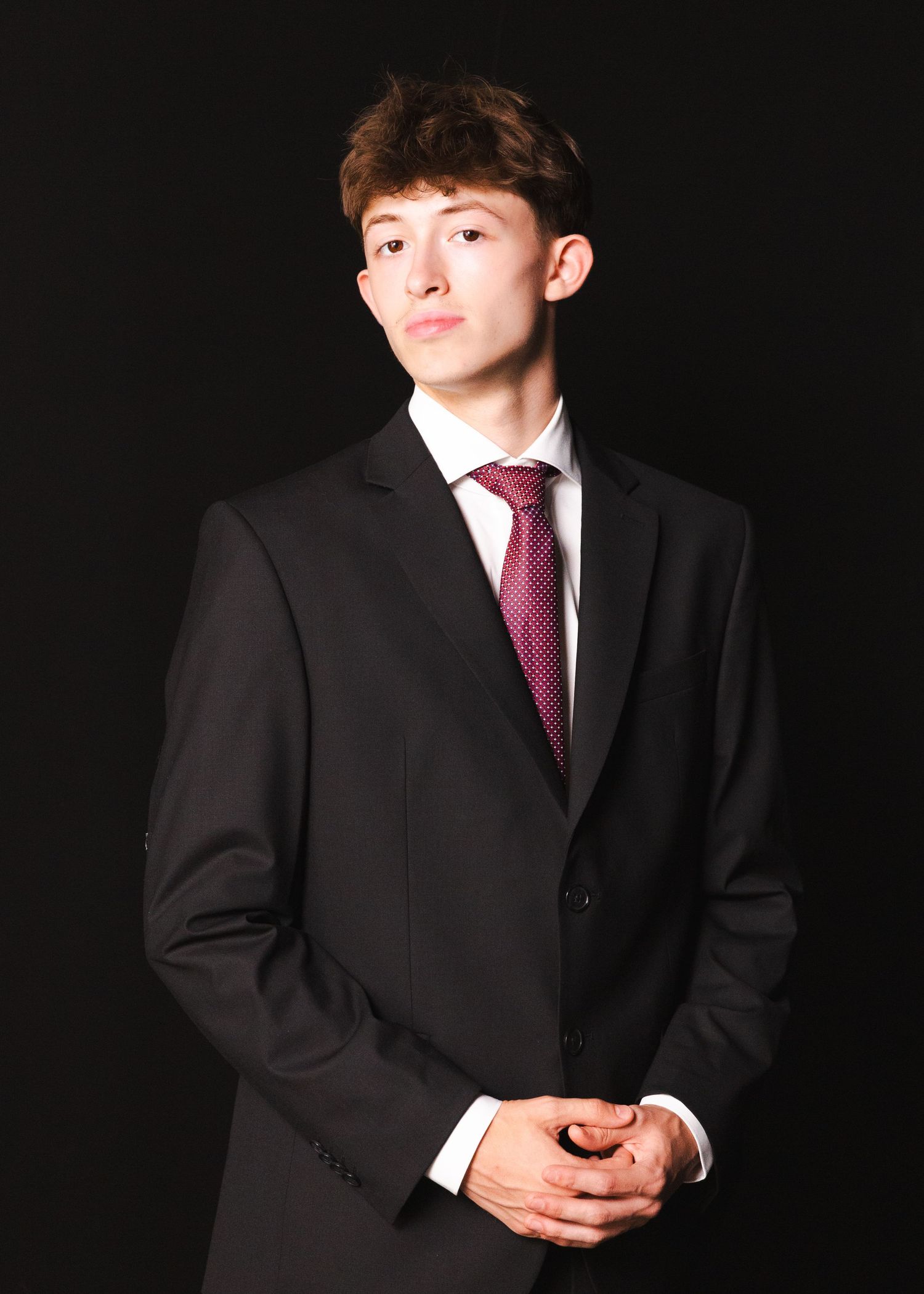 A person in formal suit and tie poses against black background.