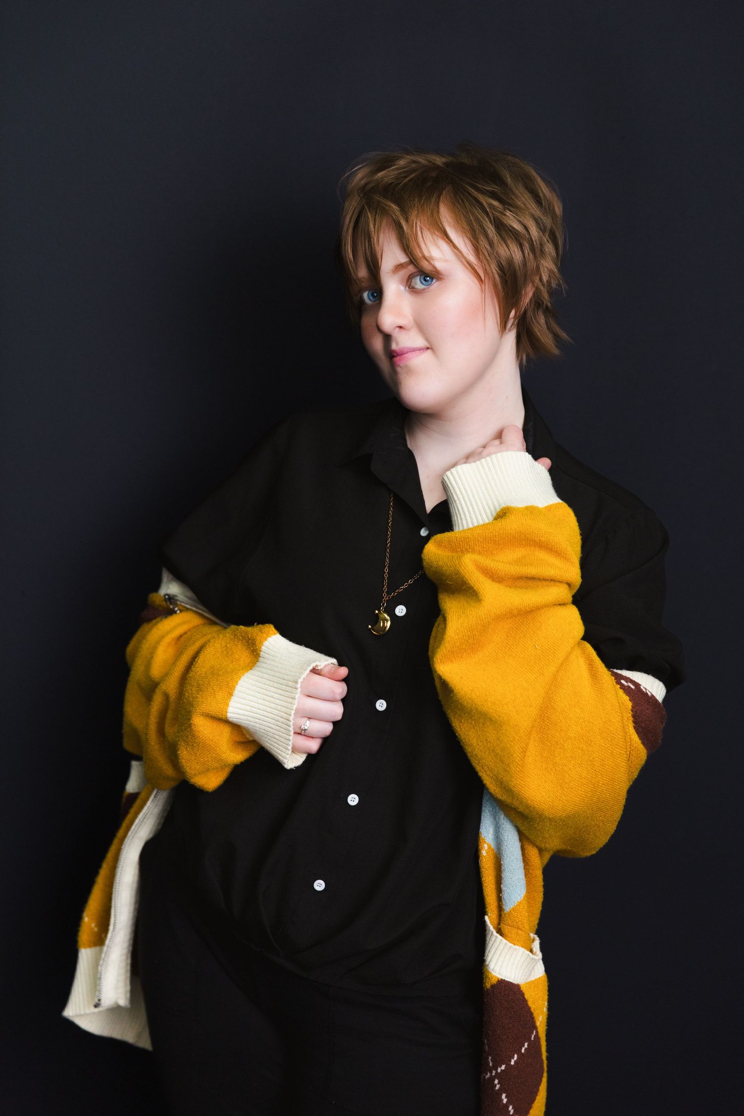 A person poses in a black and yellow jacket against a dark background.