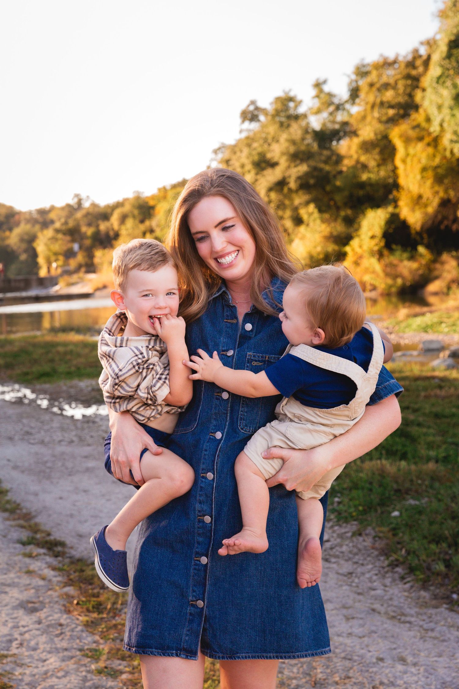 A denim-clad parent plays with young children on a sandy beach at golden hour.