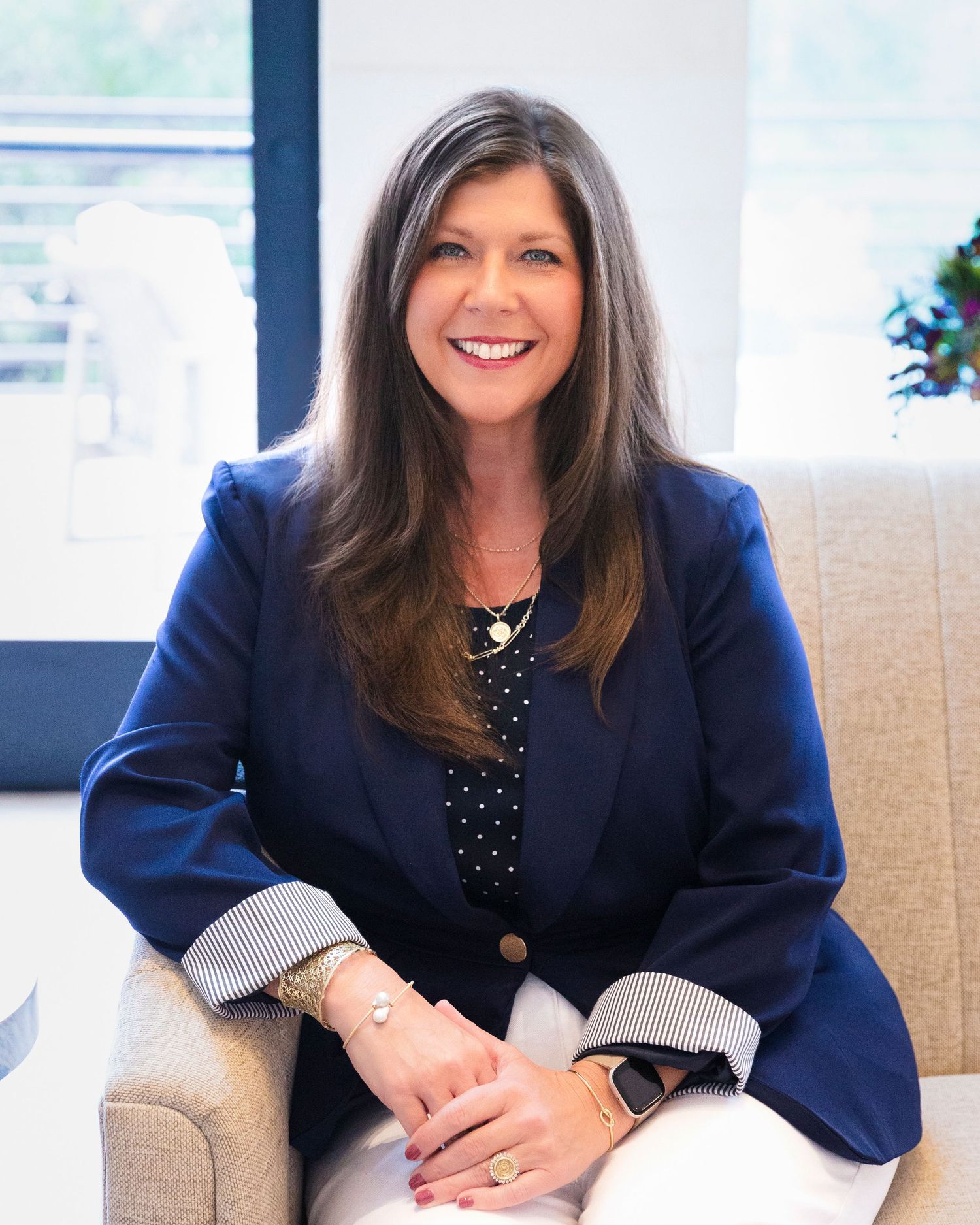 Professional business portraits in navy blazer on beige couch with natural lighting.