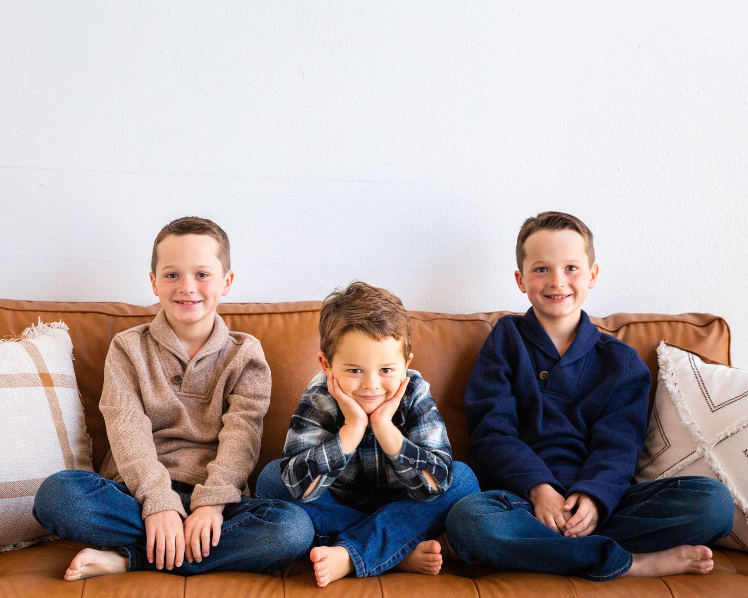 Row of children in coordinating blue and tan outfits sitting on leather furniture.