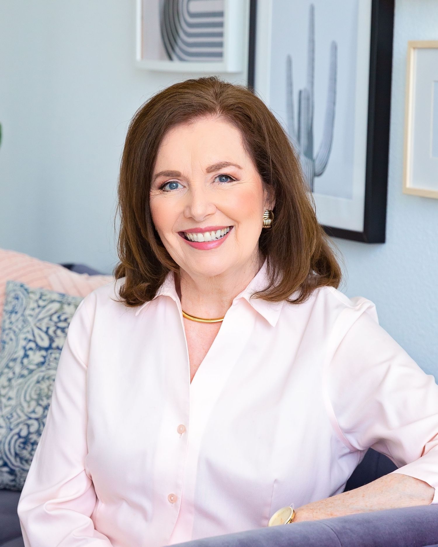 Professional headshot of woman in pink blouse seated in modern office setting.