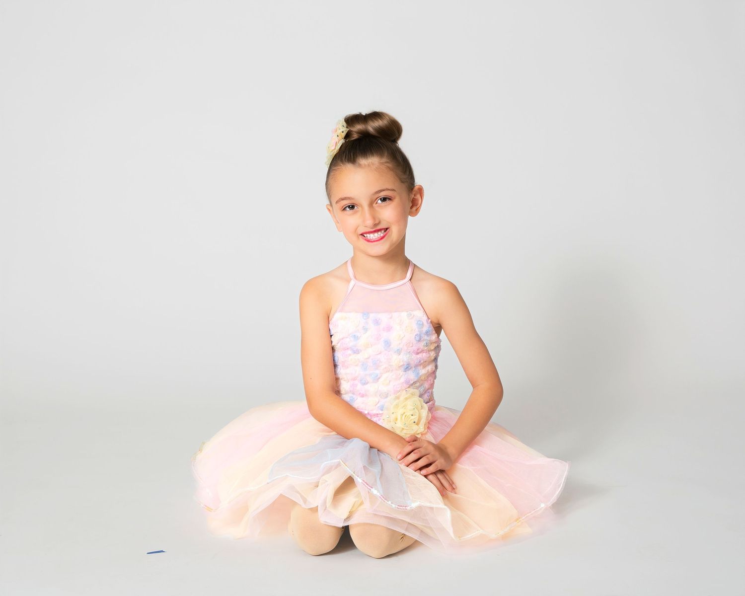 Dancer in soft pink tulle dress posing delicately on white background.