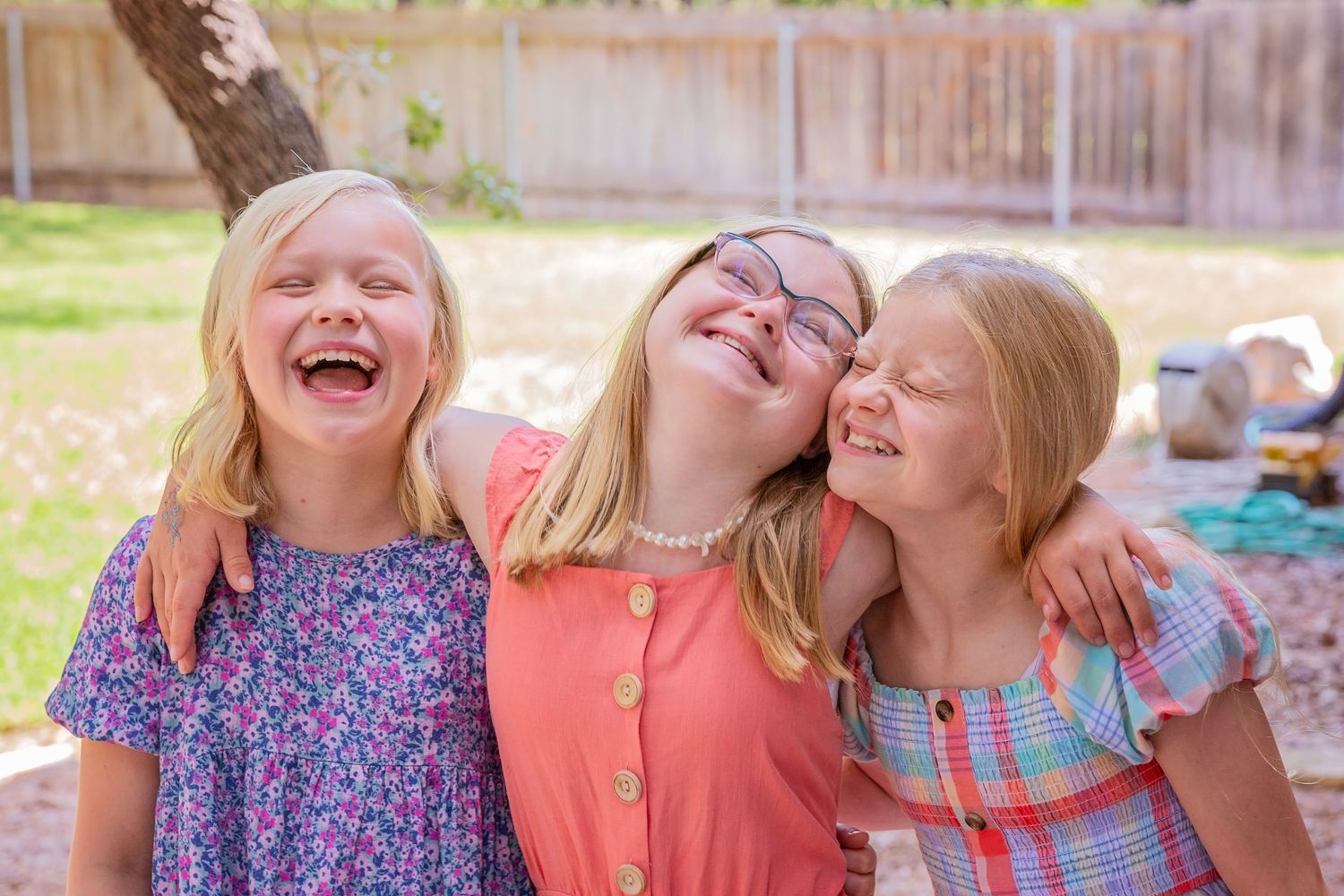 Three young girls in colorful dresses laughing and playing together outdoors.
