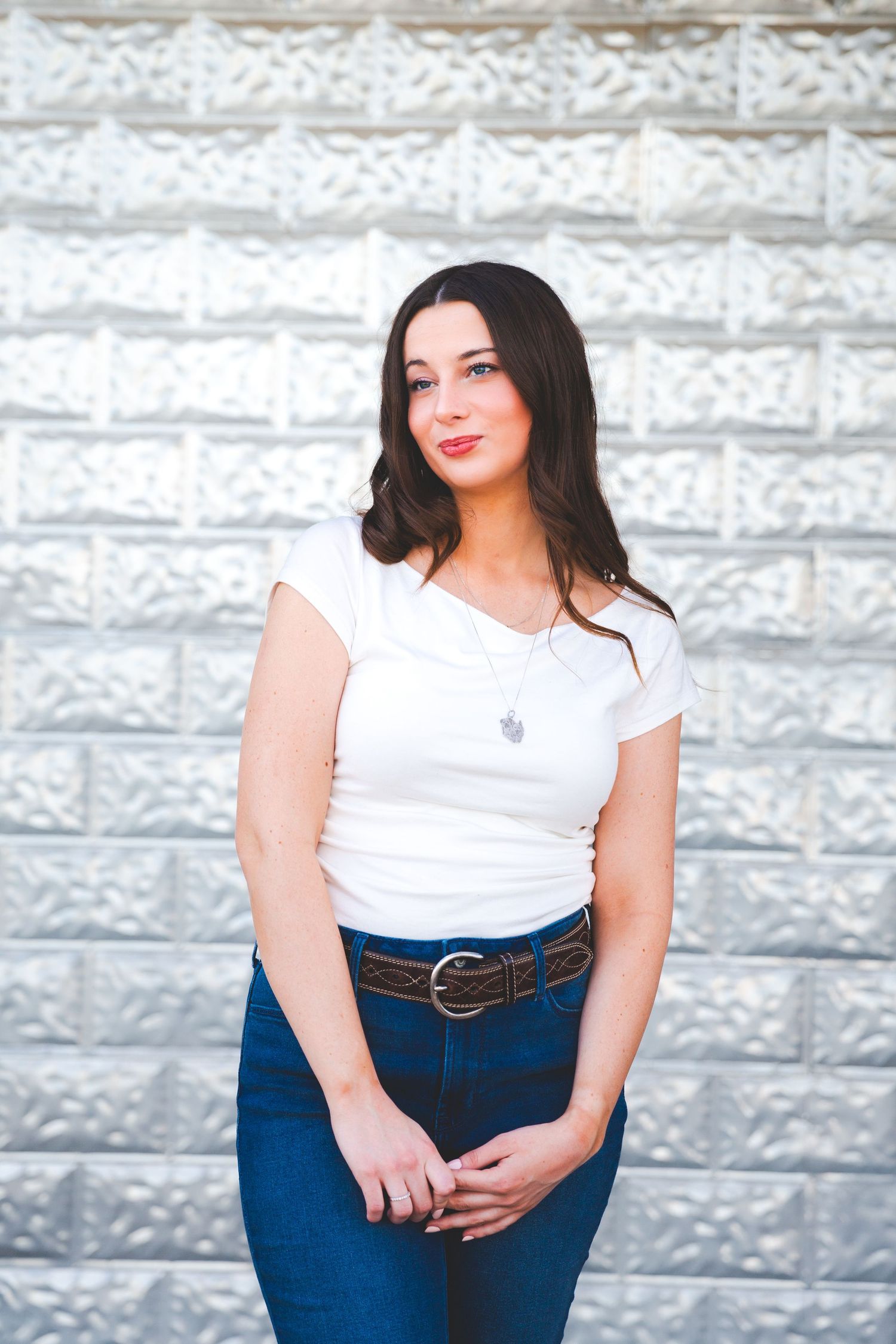 High school senior portrait session in rustin Taylor, TX. Portrait series against white stone wall featuring casual denim and white outfit.