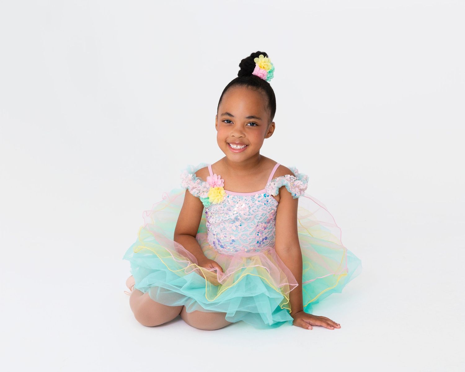 Dancer in light blue and mint tulle dress posing elegantly on white floor.