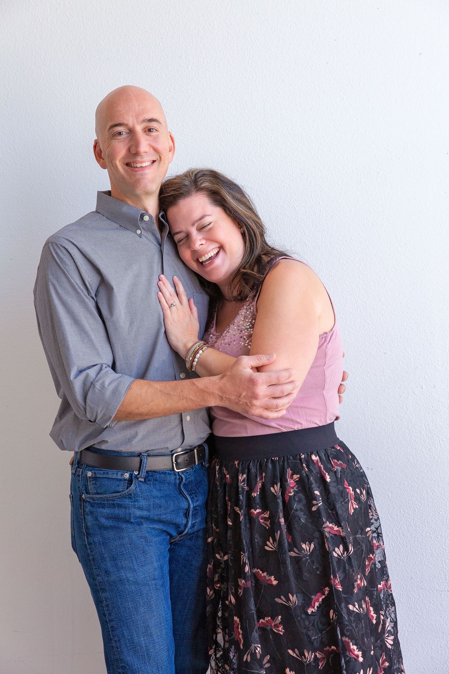 Couple shares tender moment against white studio backdrop.