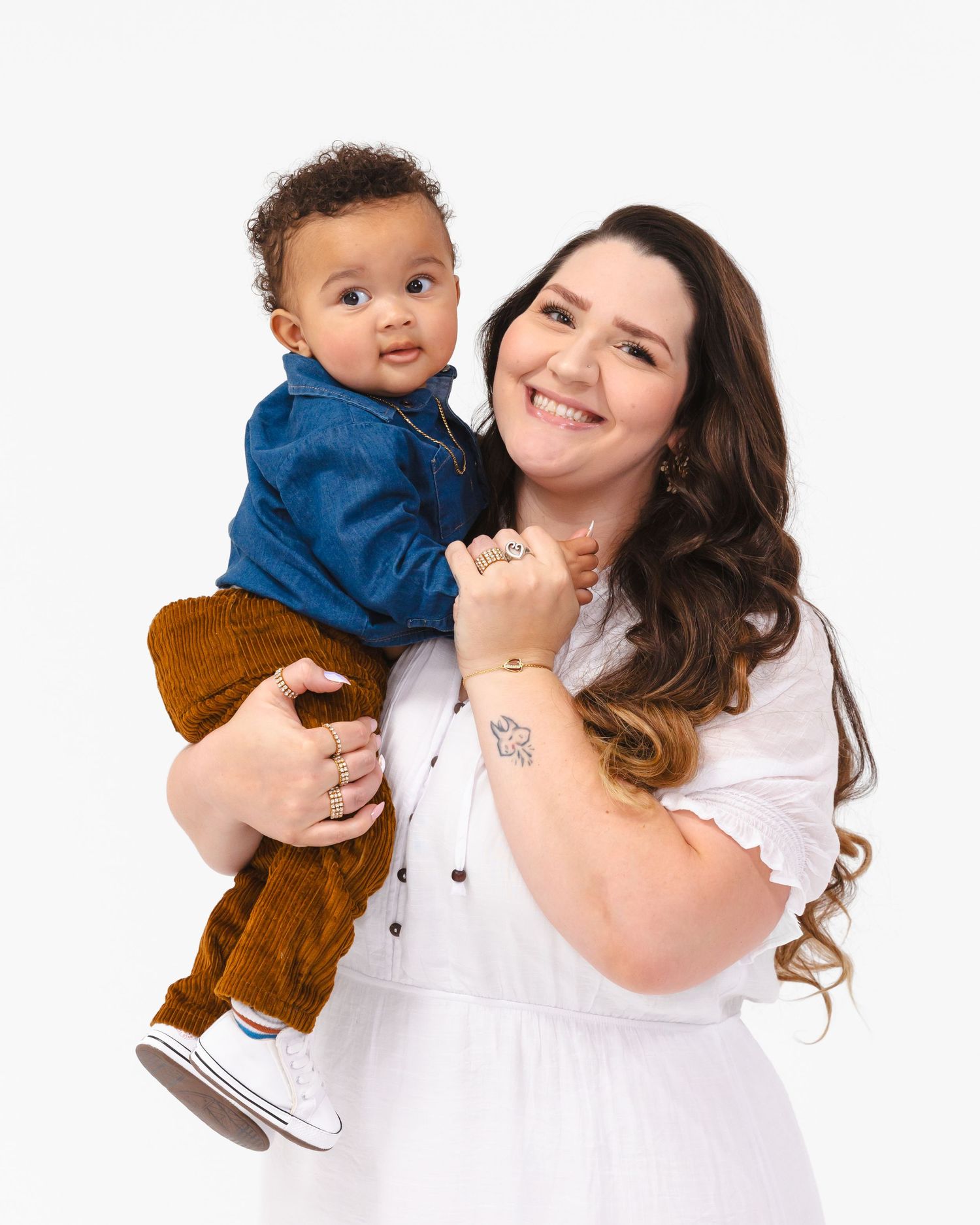 A parent holds a toddler wearing blue shirt and brown pants against white background.