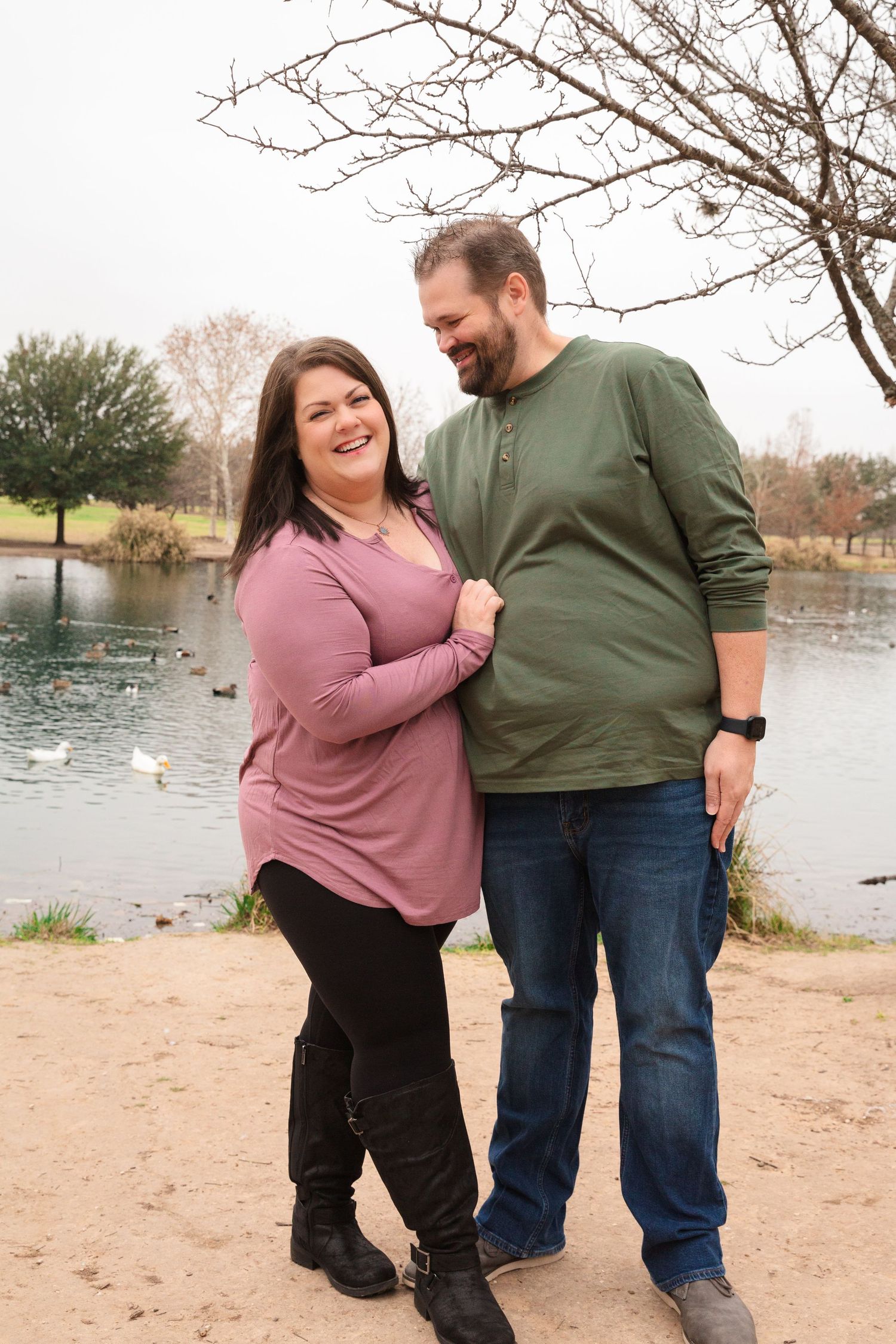 Couple poses playfully by a lake on a sandy beach during an outdoor photo session.