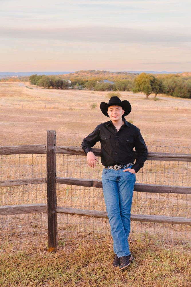 Western style portraits at sunset leaning against wooden fence in cowboy attire.