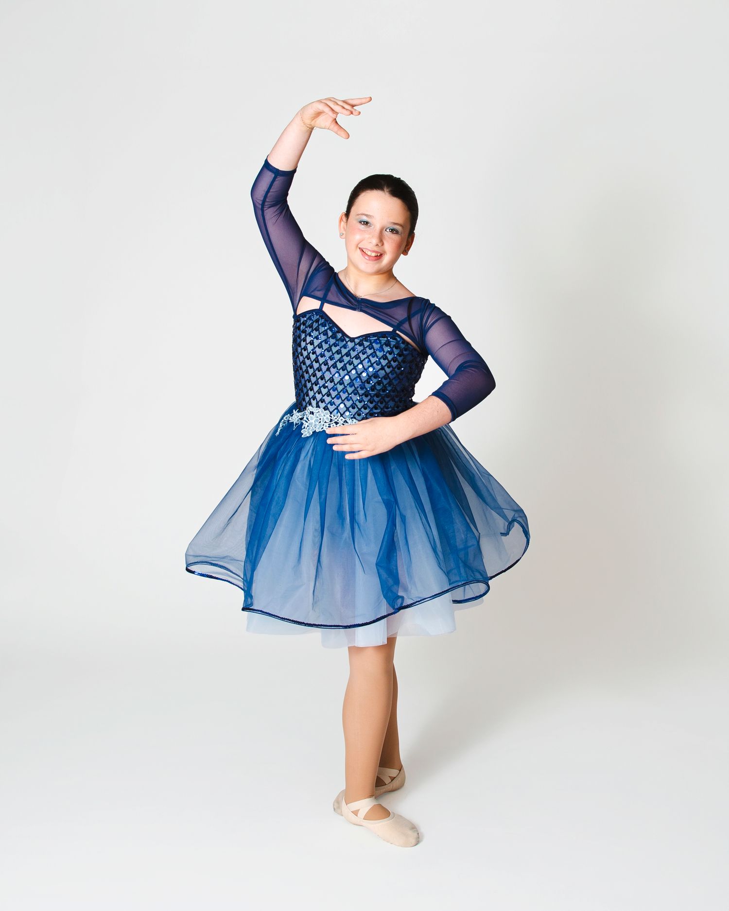 Dancer in navy blue tulle dress performing energetic movement against white backdrop.