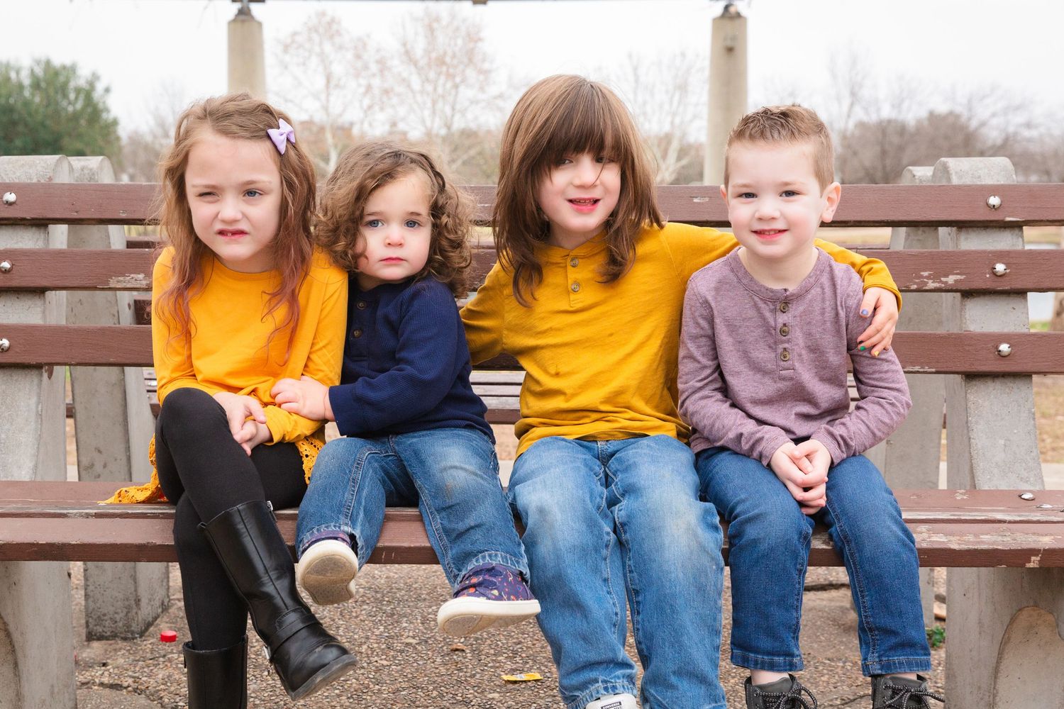 A family group sits together on a wooden bench in casual attire during an autumn day.