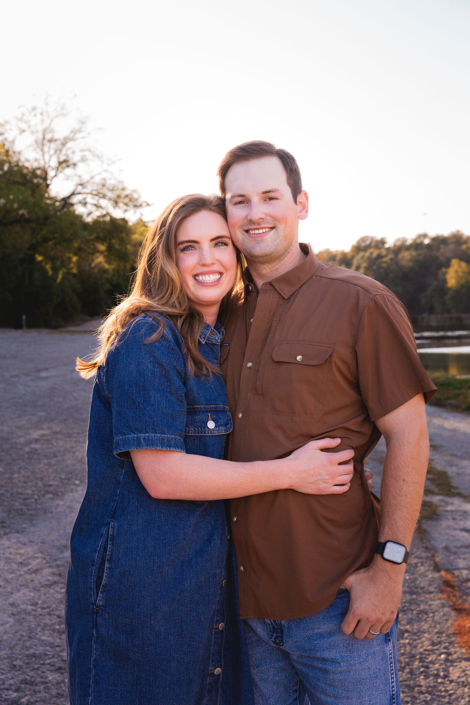 Couple in denim and brown casual wear poses during sunset photo session.