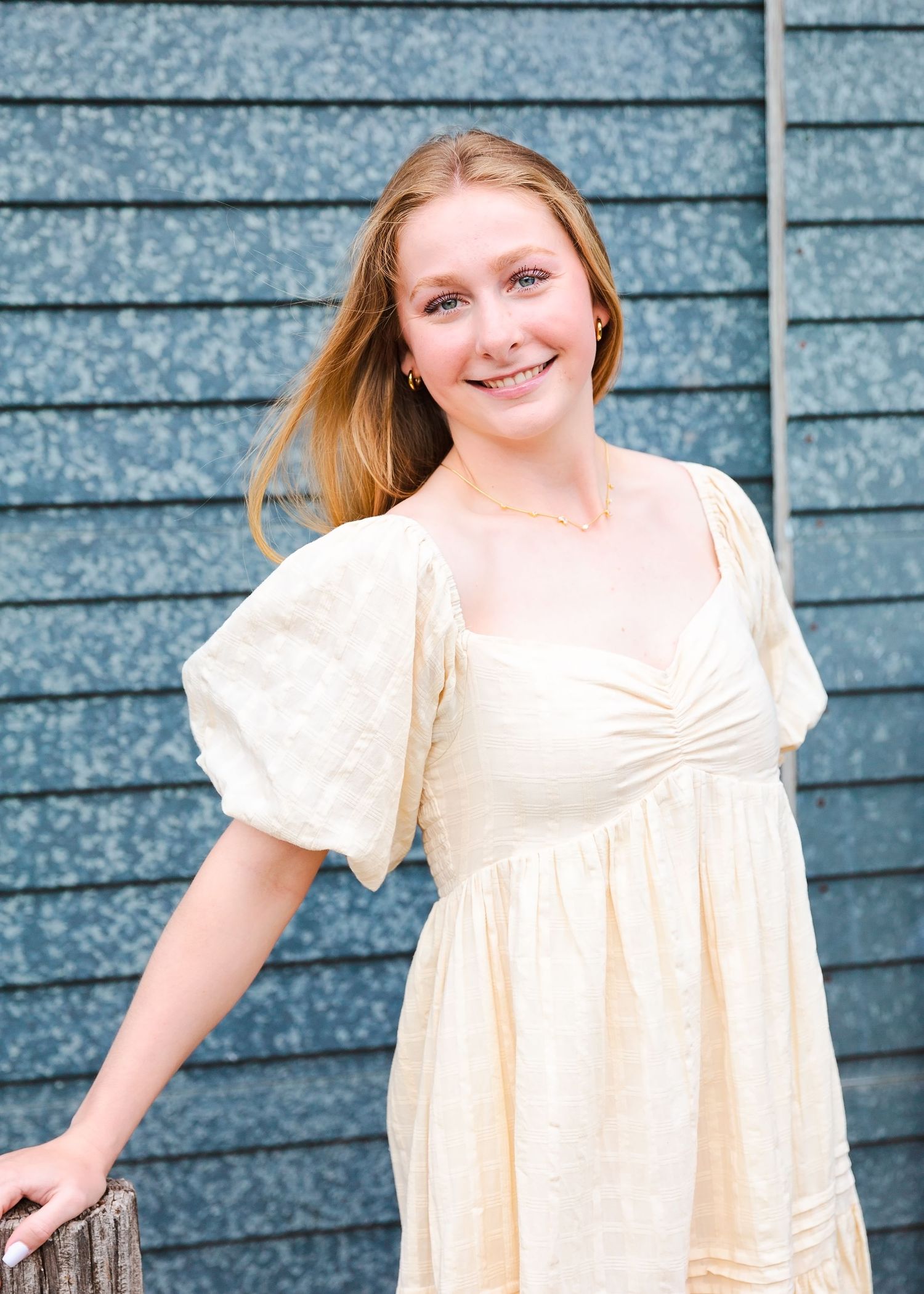 Senior Portrait in cream-colored dress with puff sleeves against blue wooden wall.